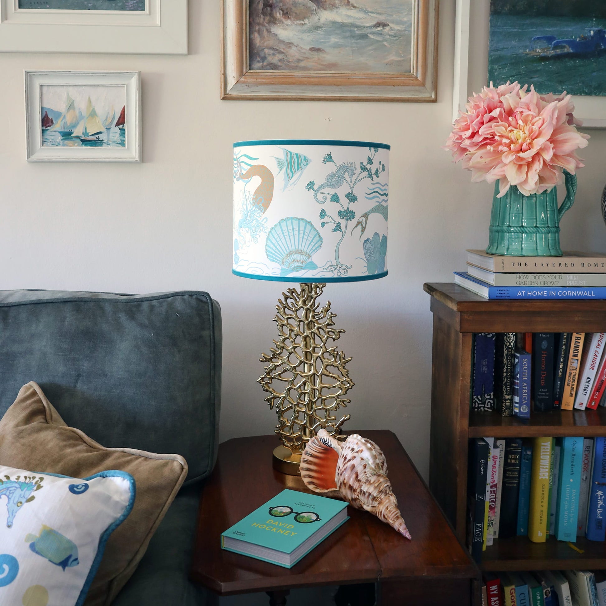 Cream Cornwall Mermaid lampshade on a gold coral lamp base, styled with coastal artwork, fresh flowers and seaside accessories in a relaxed coastal living room.