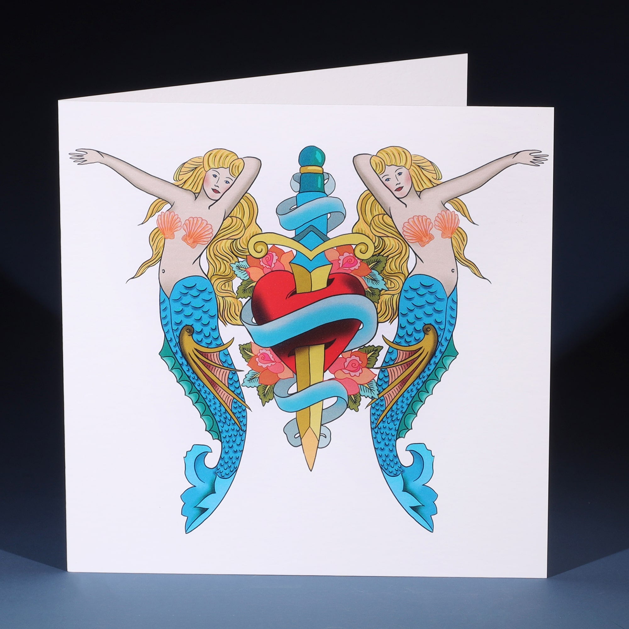 White greeting card with tattoo inspired illustration of mermaids & dagger going through a heart.