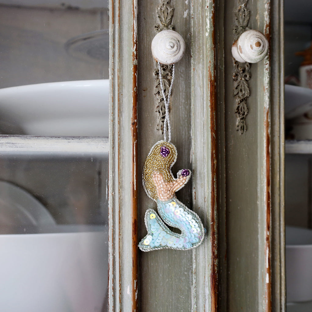 Decorative mermaid ornament hanging on a rustic wooden panel.