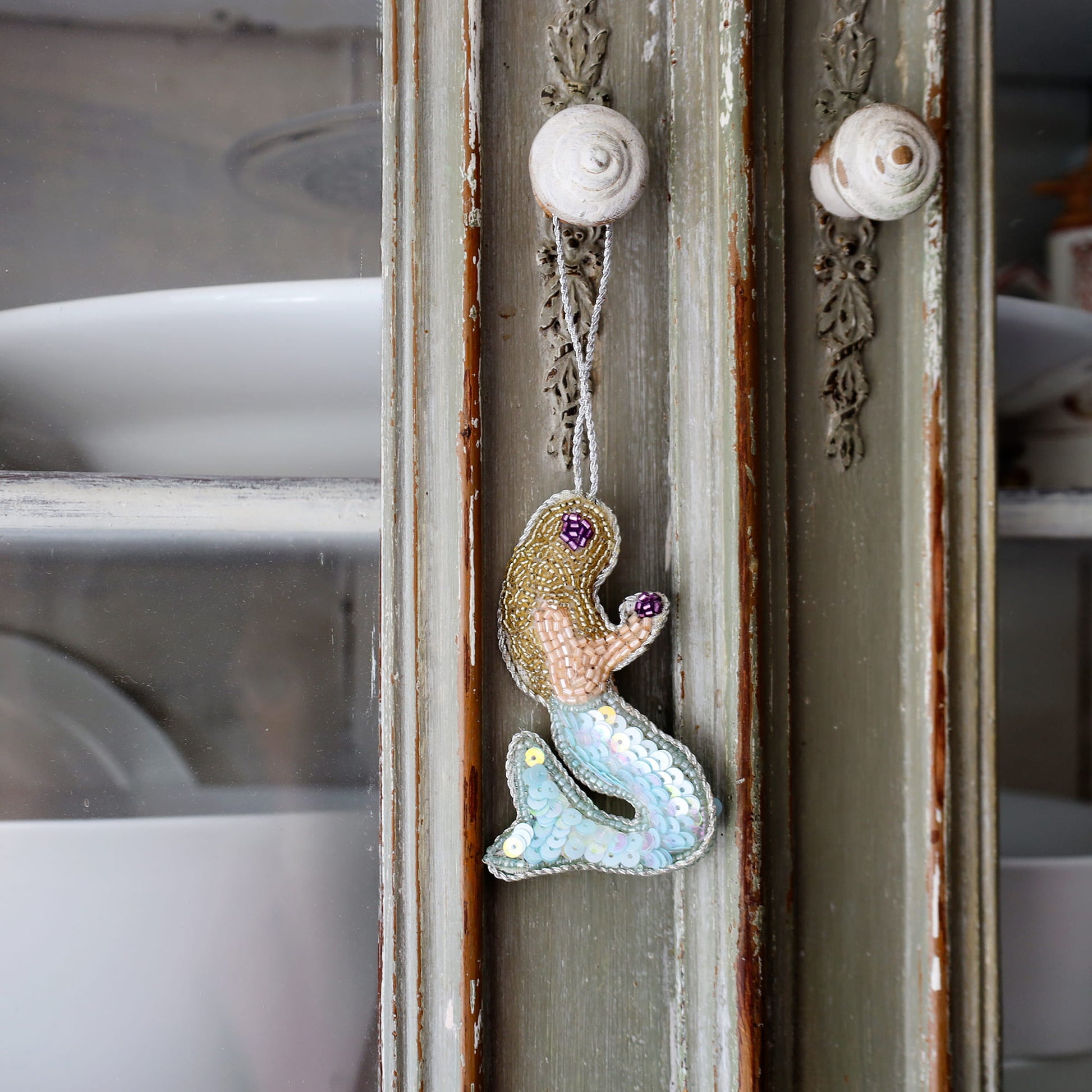 Decorative mermaid ornament hanging on a rustic wooden panel.