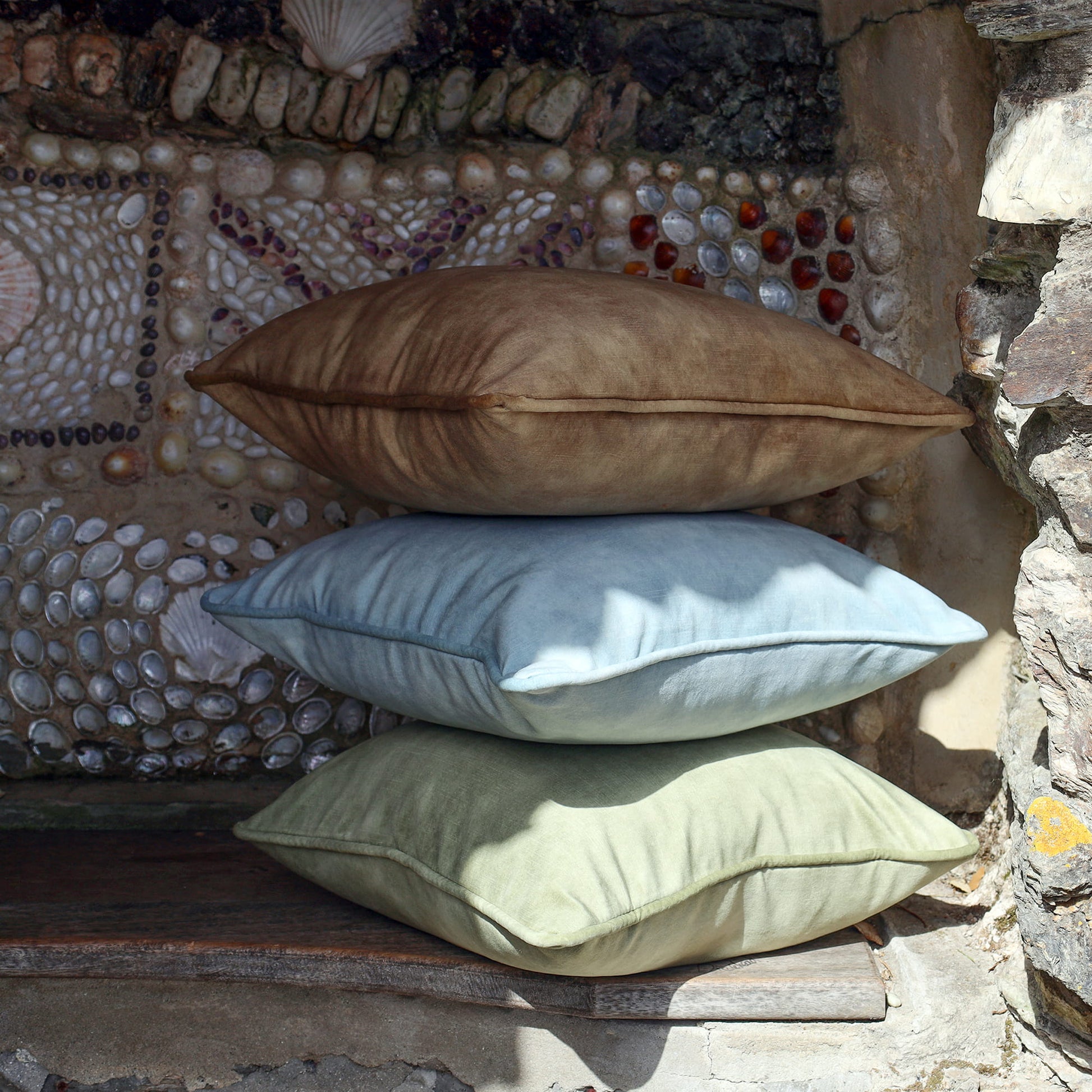 Stack of 3 velvet cushions in pale green, pale blue & gold in a shell grotto.