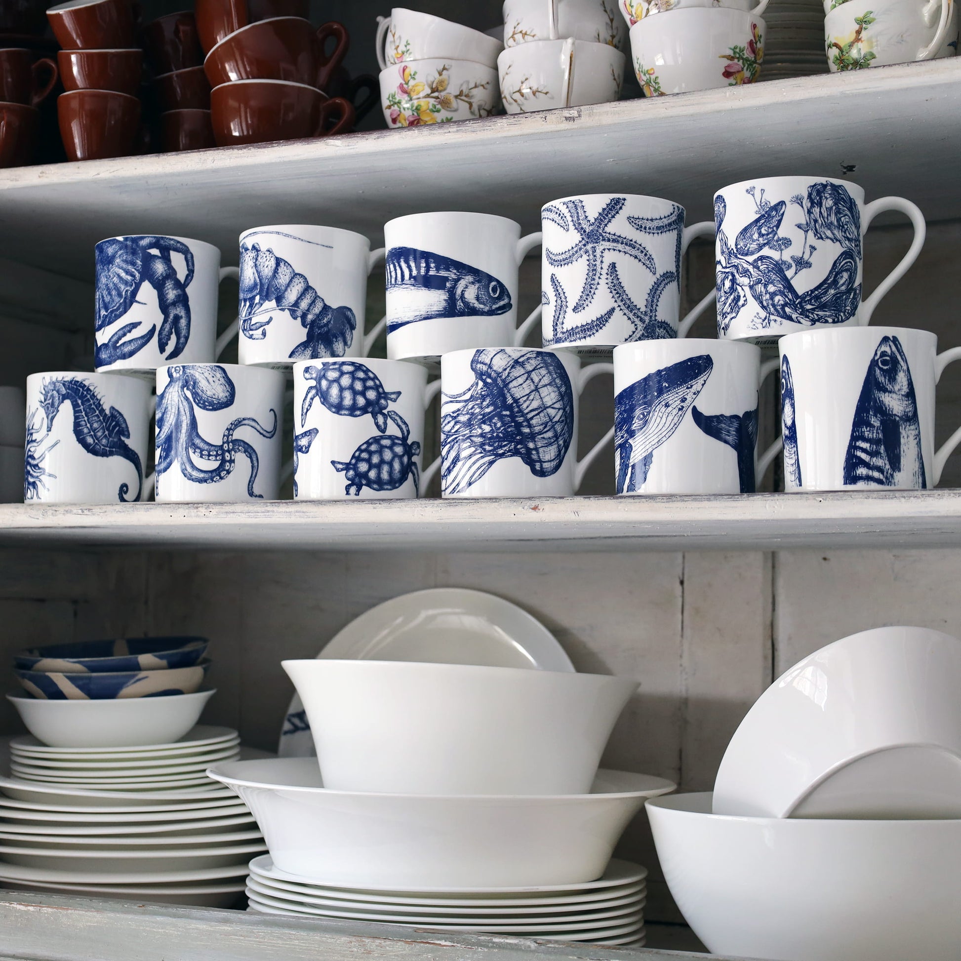Shelves with white ceramic mugs and bowls featuring blue animal designs.