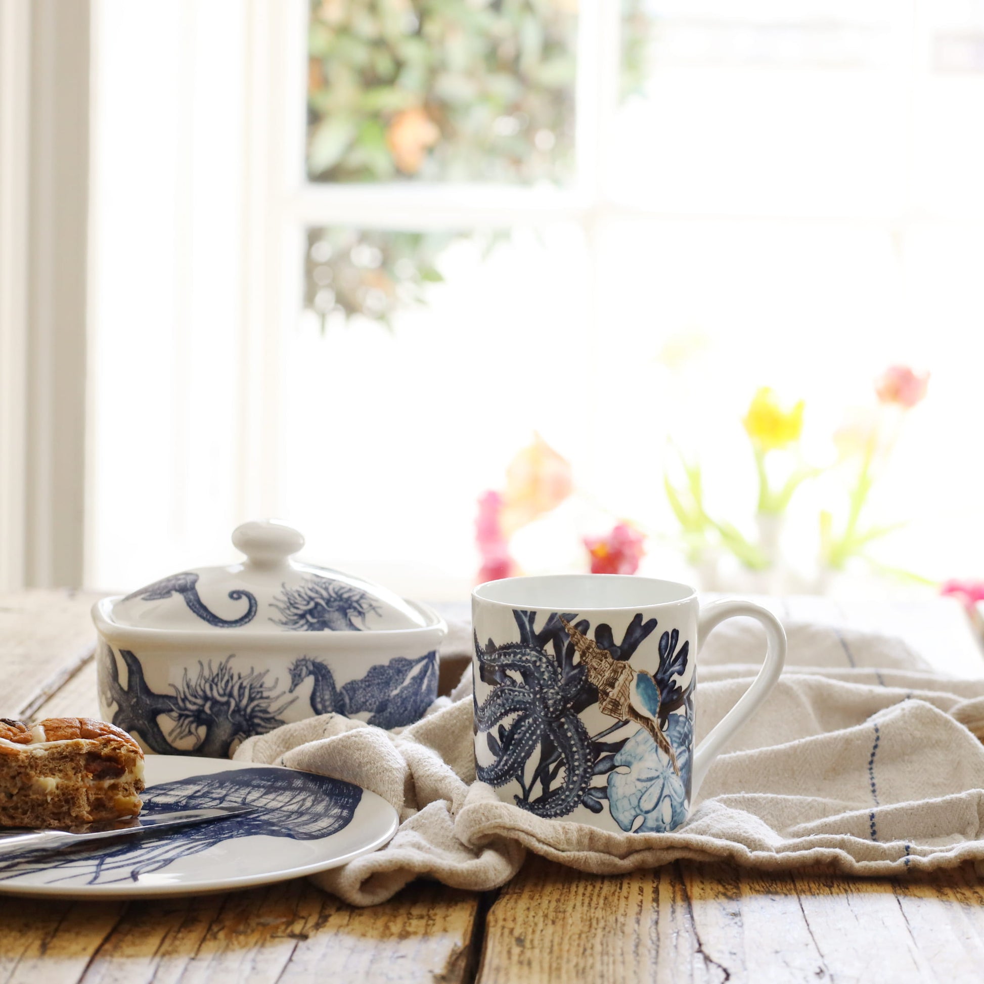 Ceramic mug with blue beachcomber design on a wooden table, with a blurred window background.