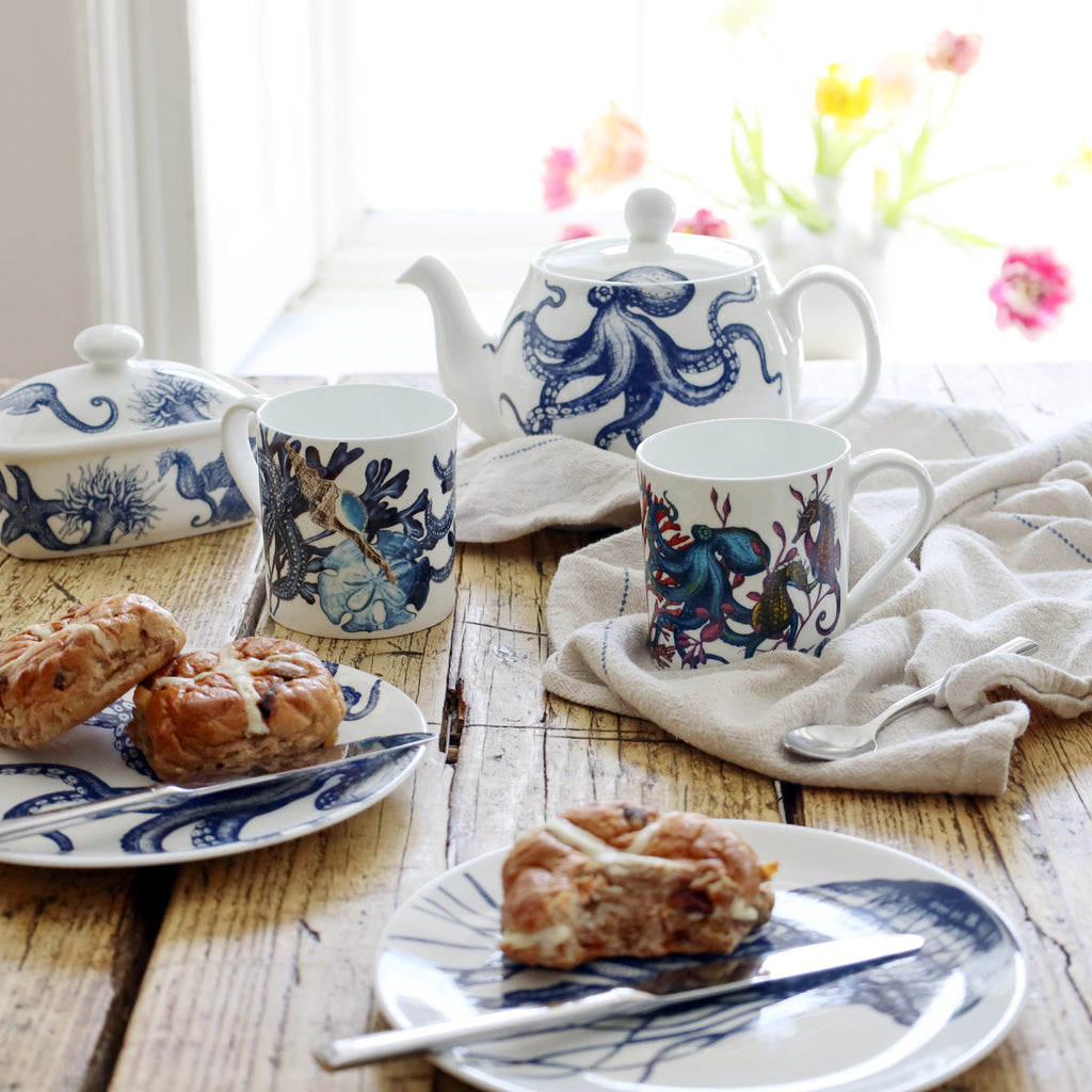 Tea set with blue and white octopus design on a wooden table with pastries.