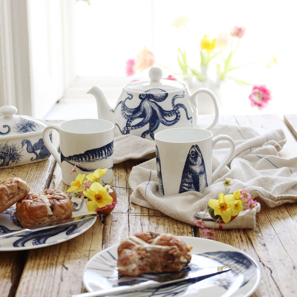 Tea set with blue and white designs on a wooden table with pastries and flowers.