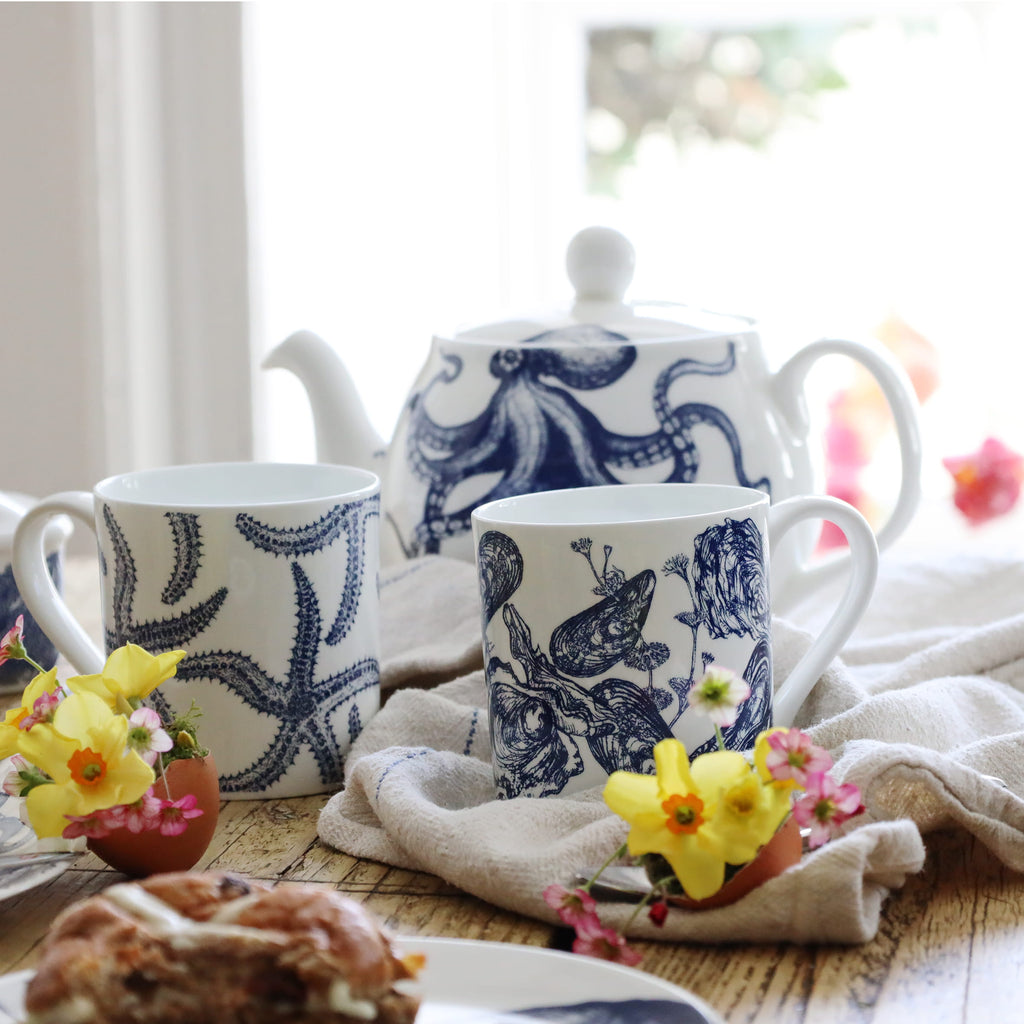 Tea set with blue and white designs on a wooden table with flowers.