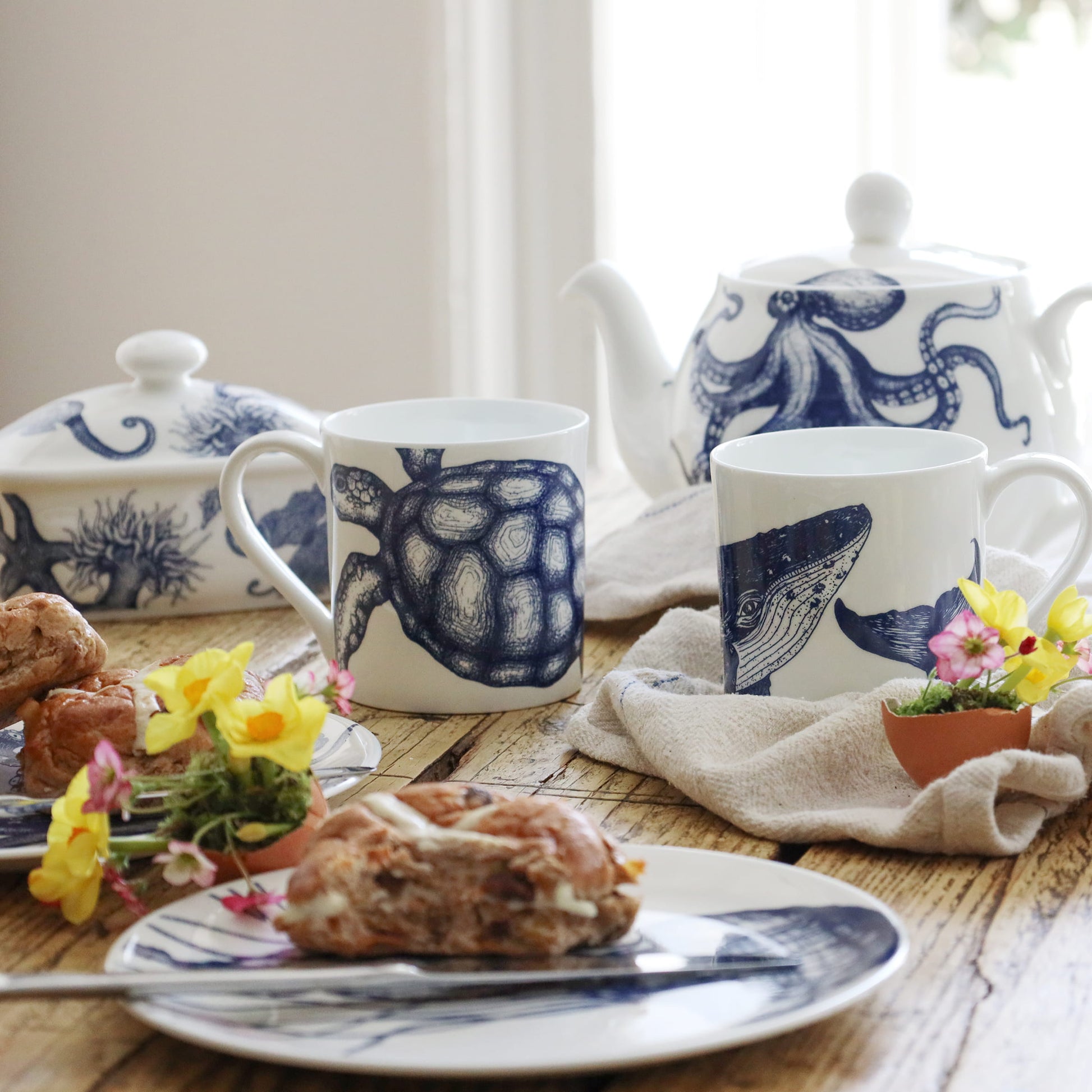 Tea set with blue and white animal-themed mugs and teapot on a wooden table.