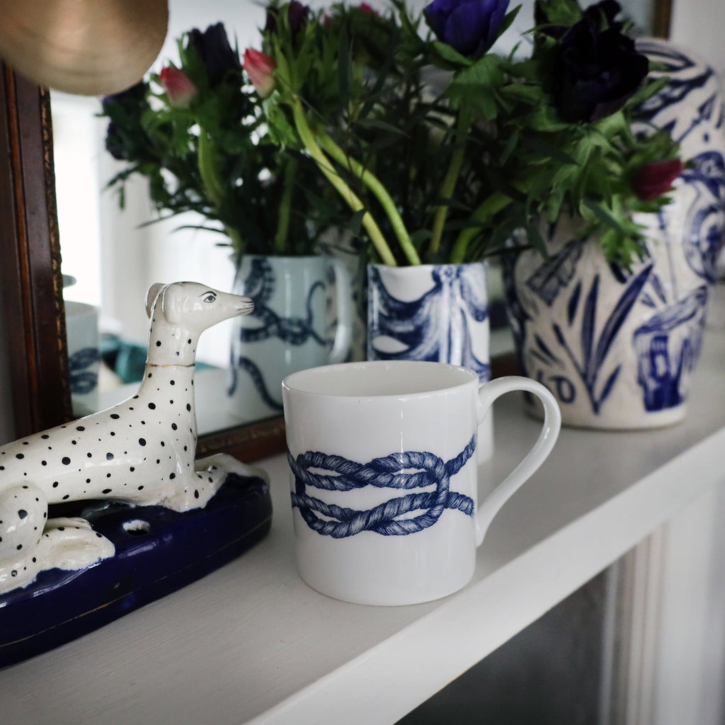 reef Knot  Mug on a mantlepiece with an octopus jug containing flowers.Also on the mantlepiece is a statue of a spotted dog and a blue & white lidded Jar in front of a mirror.
