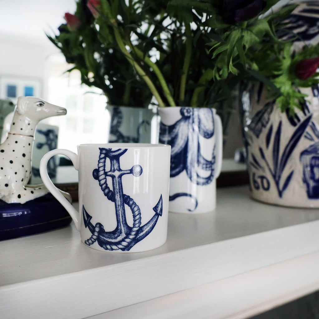 Anchor Mug,with a twisted rope on a mantlepiece with an octopus jug containing flowers.Also on the mantlepiece is a statue of a spotted dog and a blue & white lidded Jar in front of a mirror.