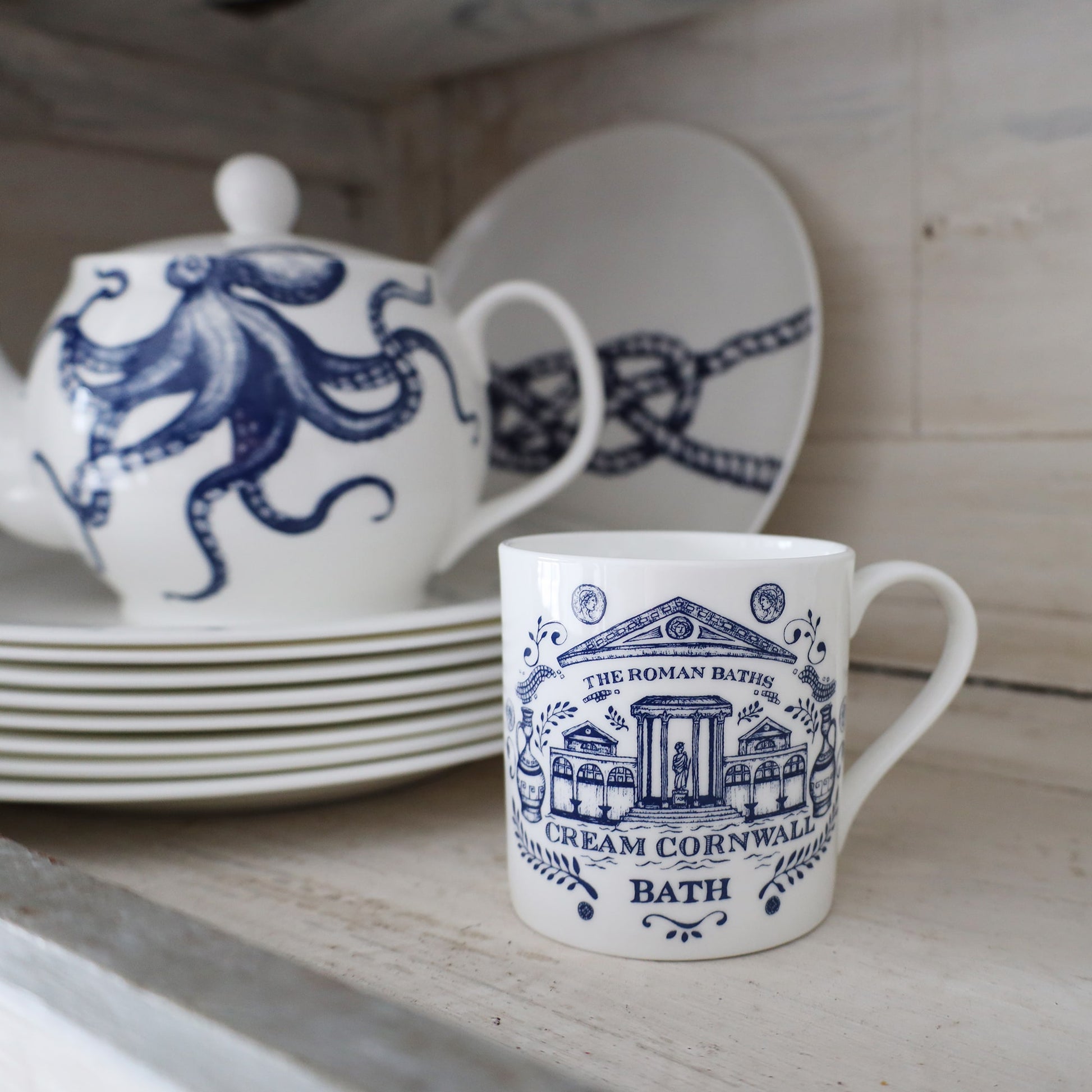 Bath Mug on a white washed shelf next to an Octopus Teapot plated on a stack of plates