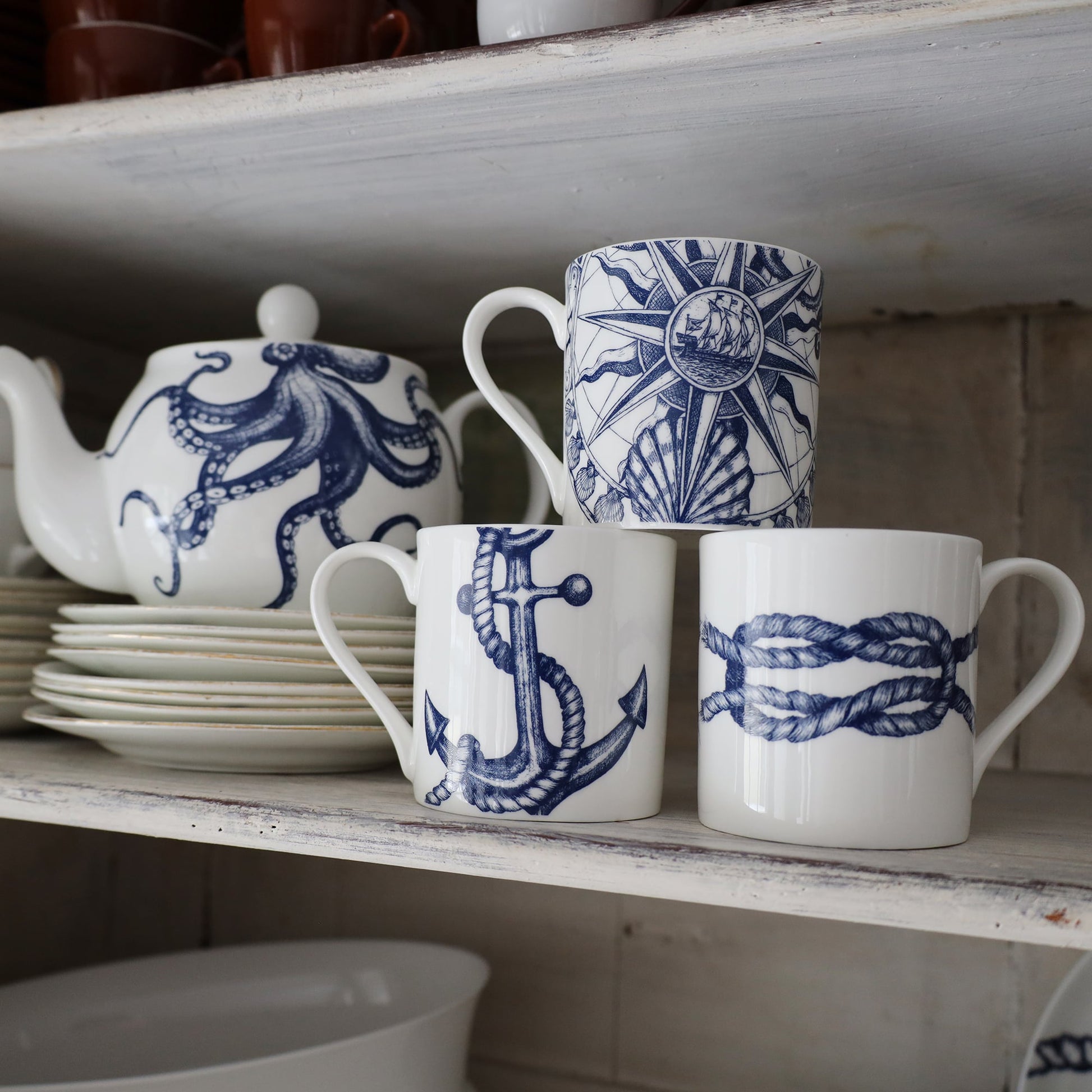 Compass mug place on a stack of Reef Knot and Anchor  Mugs next to an Octopus Teapot the mug  is on a stack of small white plates. 