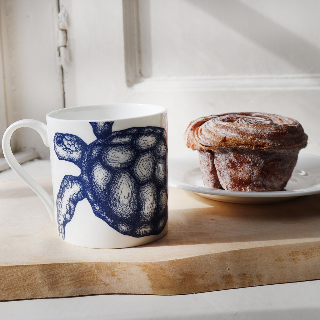 Turtle mug placed on a wooden board next to a plate with a Cinnamon bun