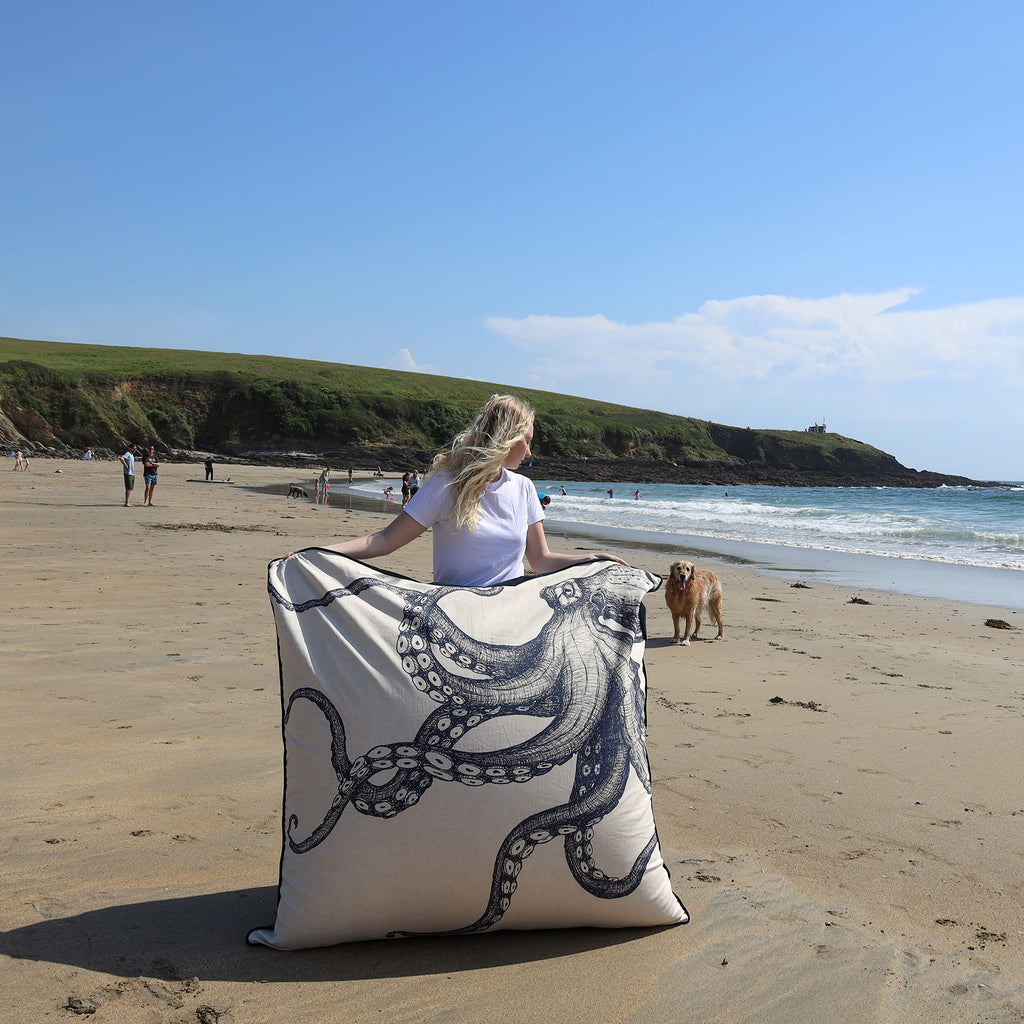 Person holding a decorative pillow with an octopus design on a beach