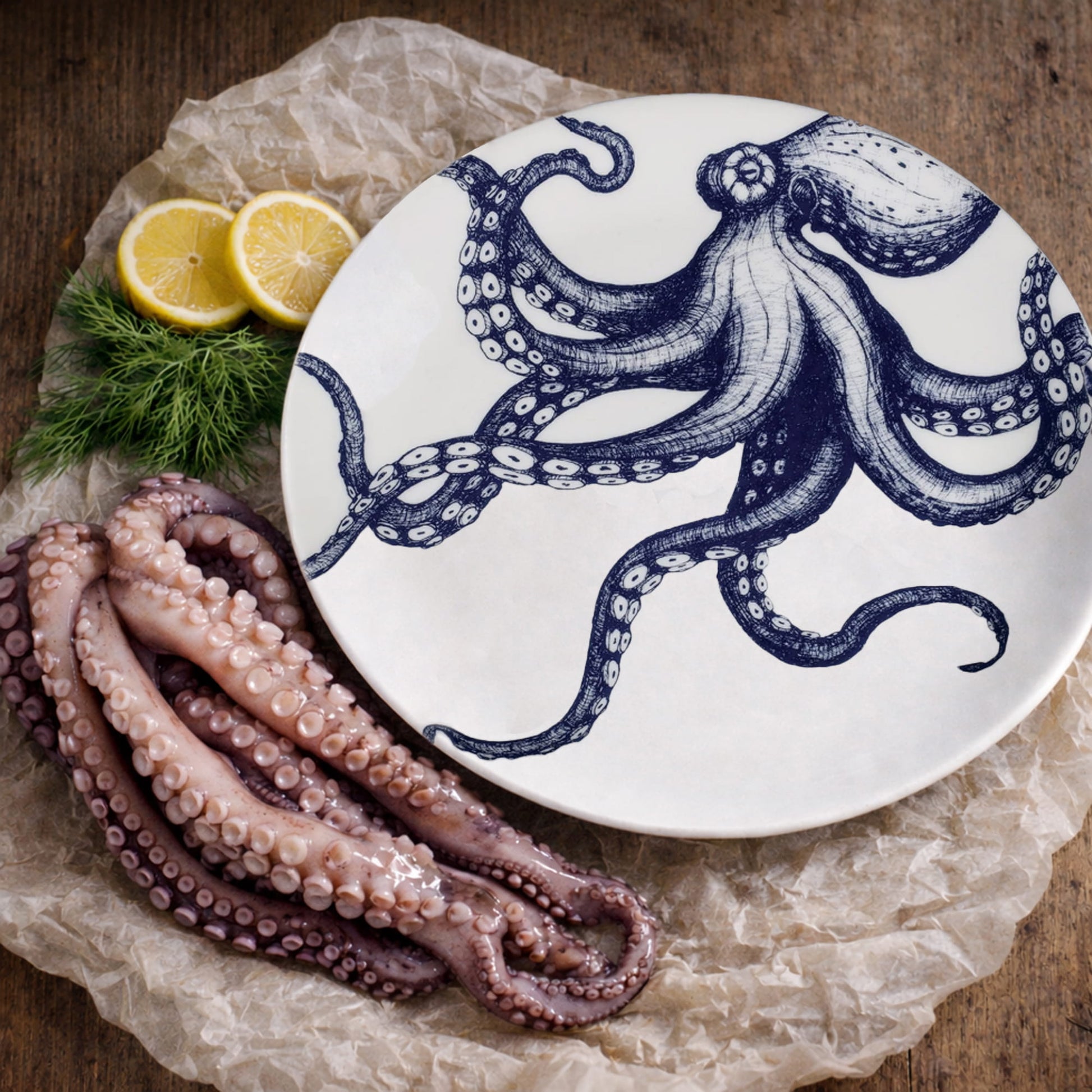 White plate with blue octopus design, fresh octopus tentacles, and lemon slices on a wooden surface.