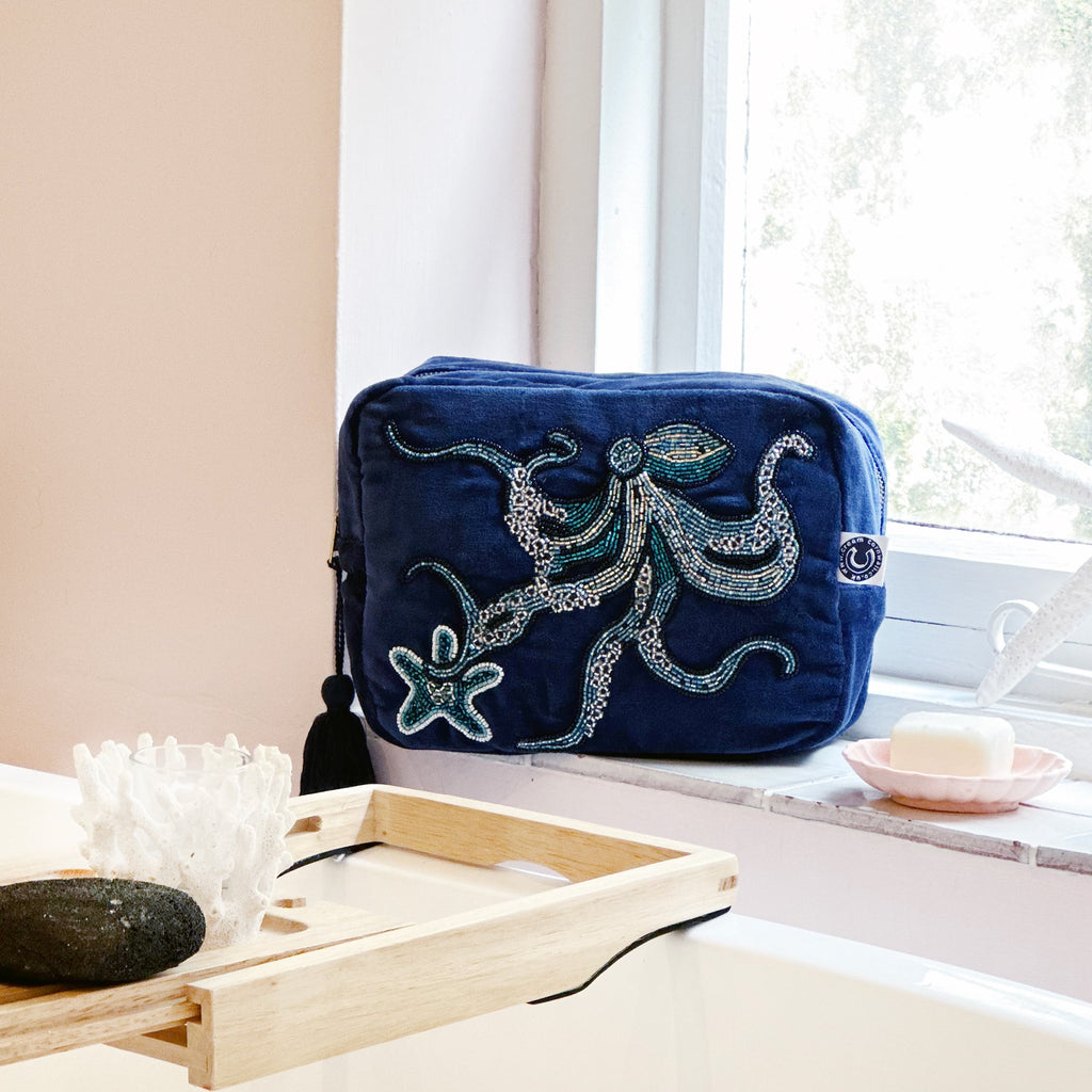 Beaded navy velvet wash bag with octopus and starfish decoration on the front sitting on a bathroom window ledge with the sun coming through.
