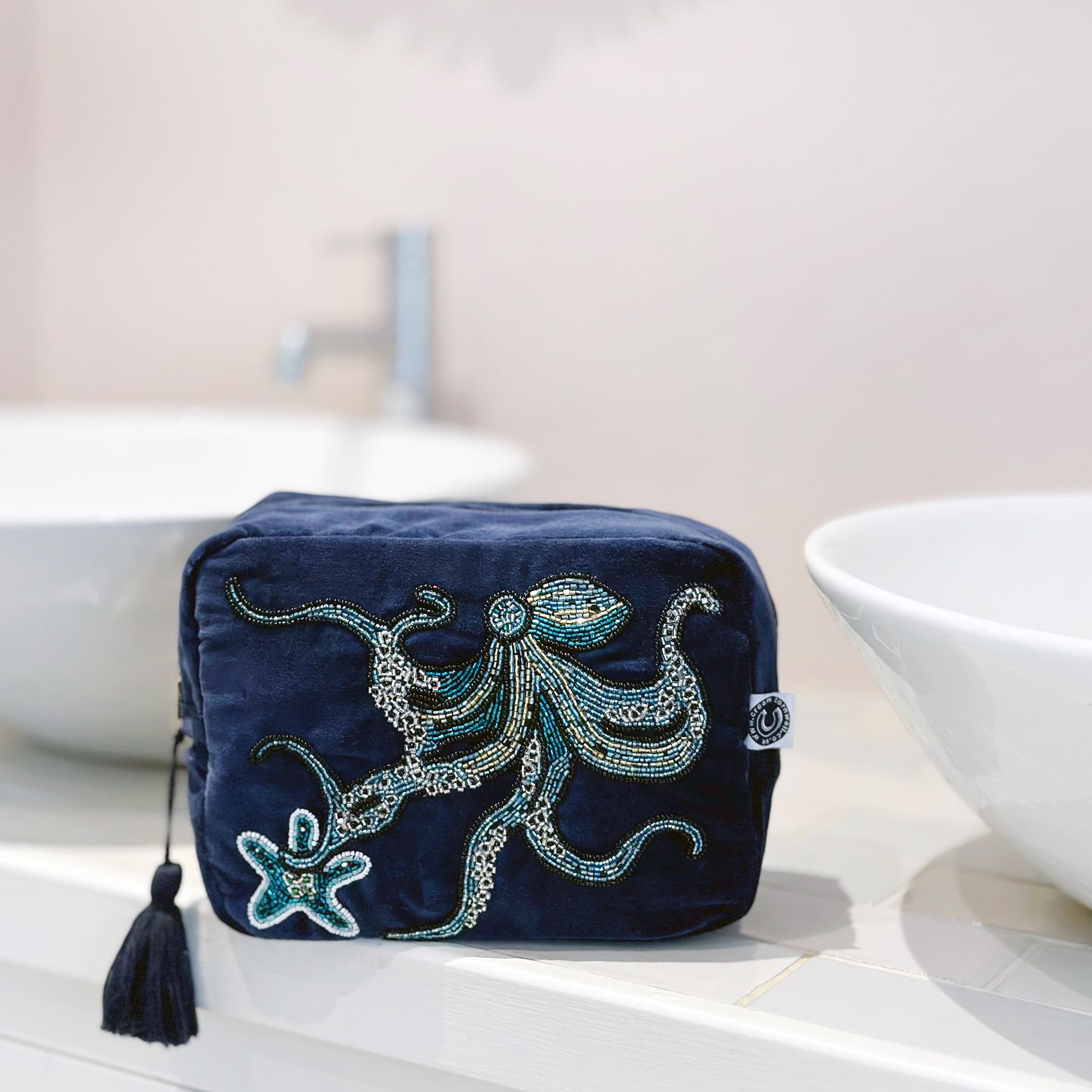 Beaded navy velvet wash bag with octopus and starfish on the front. The bag is sitting on a tiled bathroom worktop in between 2 round basins.