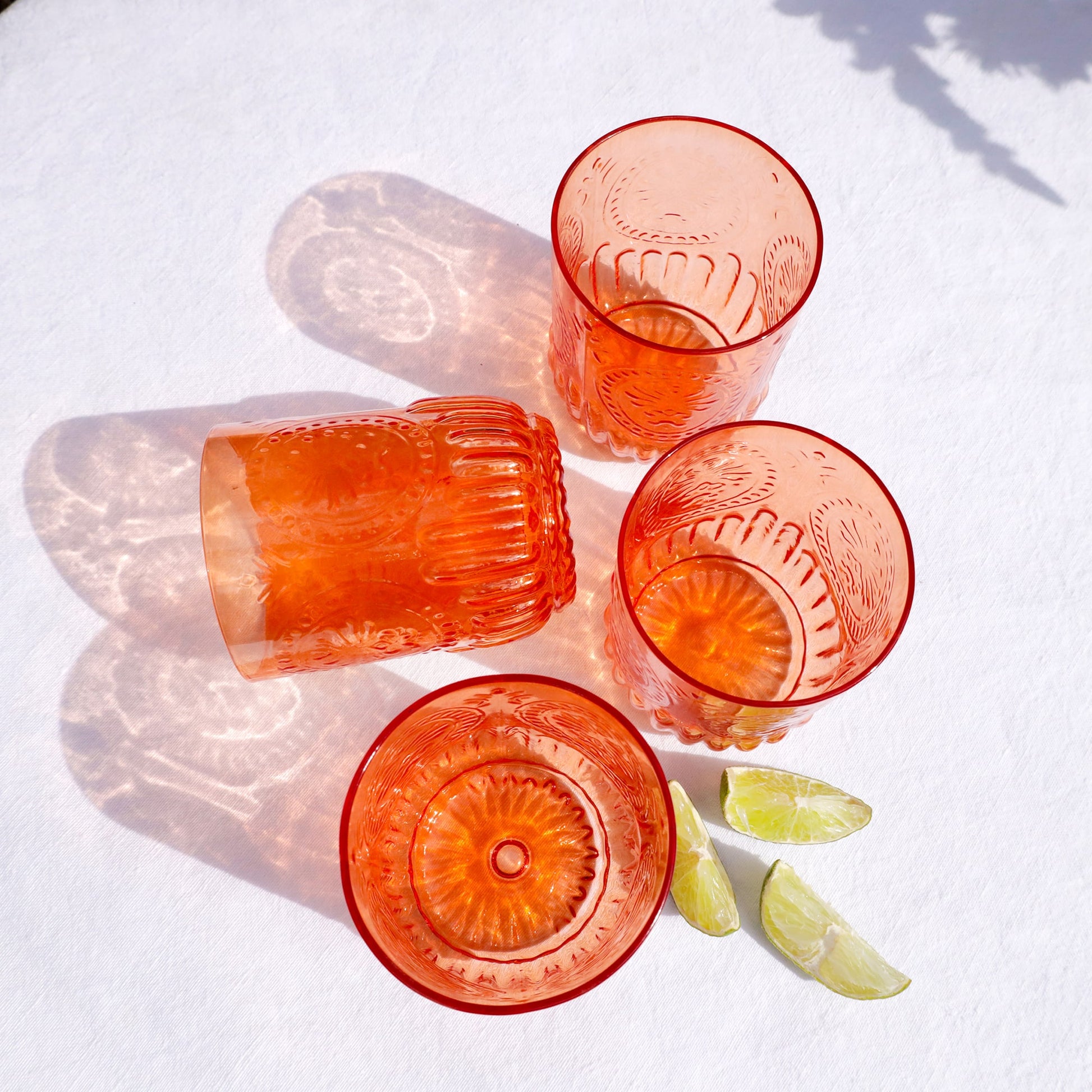 Set of red glass tumblers on a white surface with lime wedges.