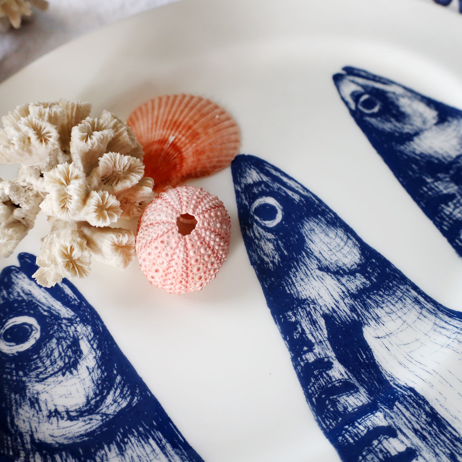 Decorative plate with blue mackerel heads patterns, coral, and shells on a white surface.