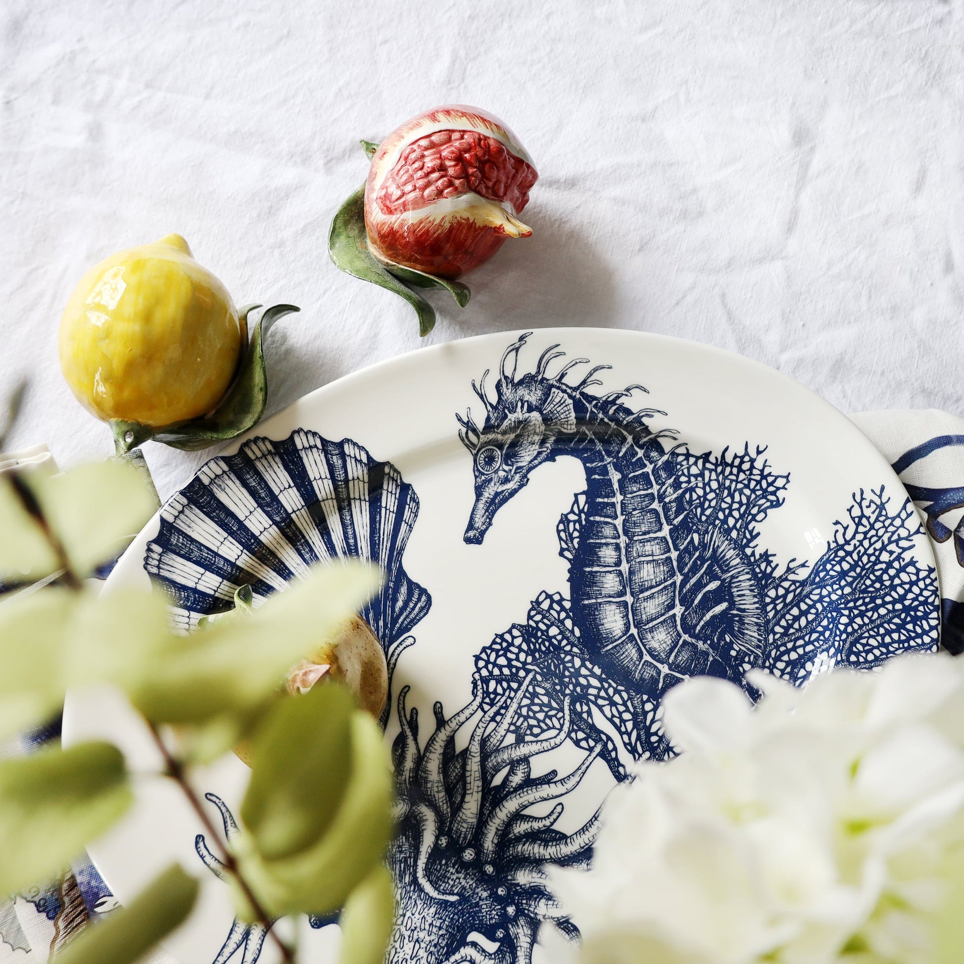 Decorative plate with blue seahorse design on a white surface with fruits and flowers.
