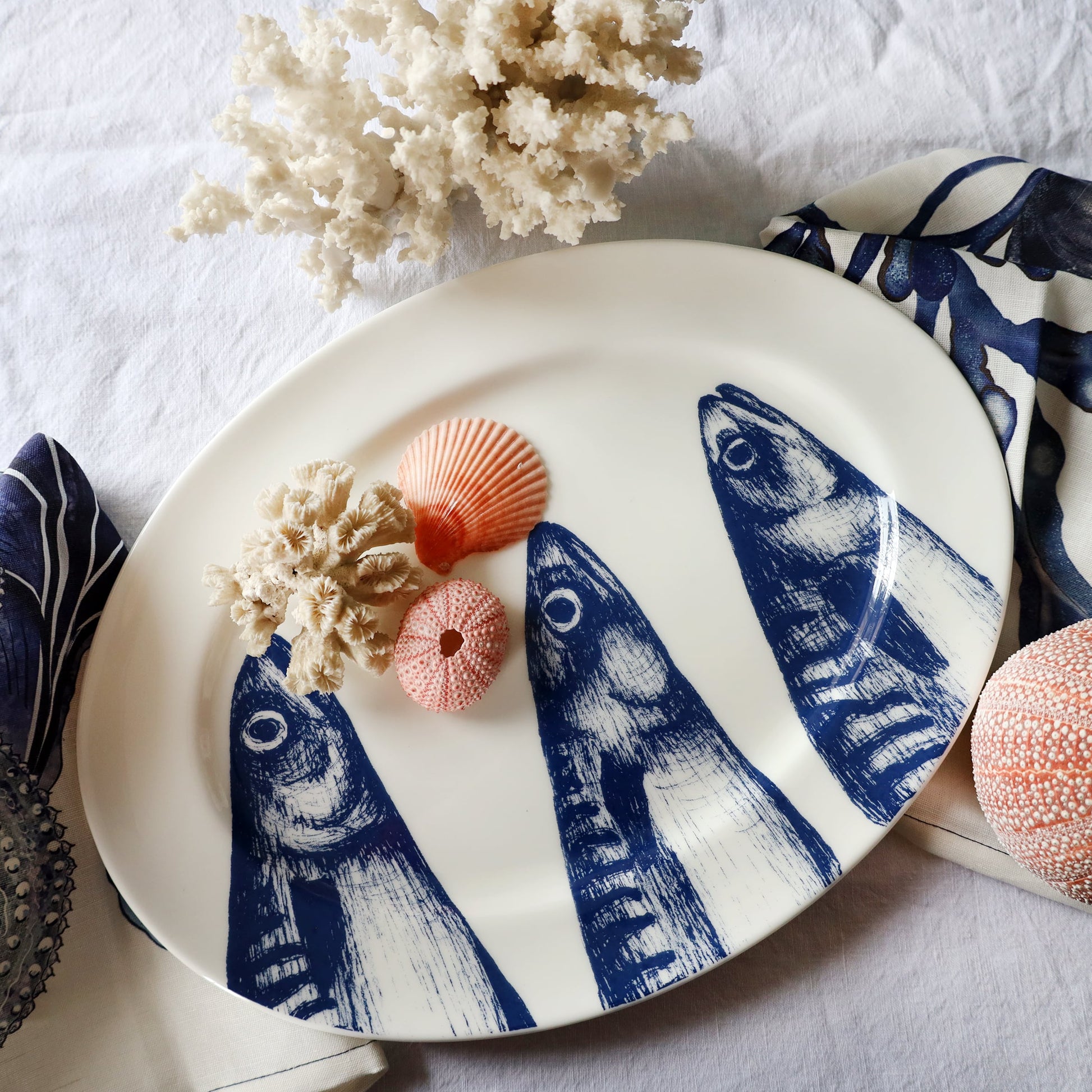 Decorative plate with blue fish design on a white surface with coral and shells.