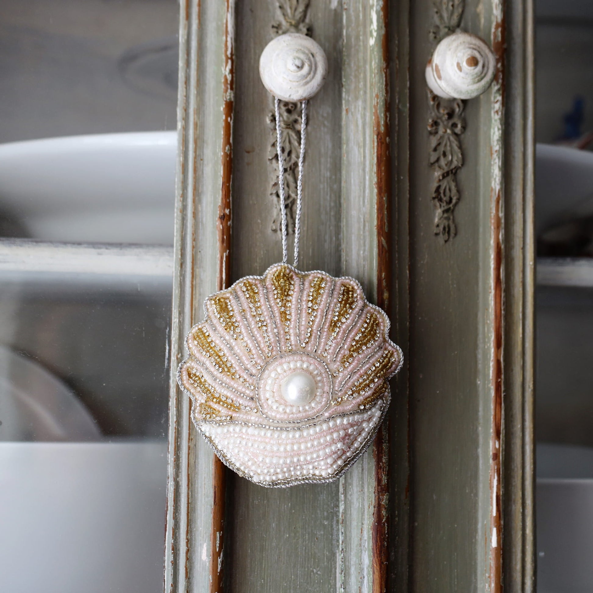 Decorative shell ornament with beads hanging on a textured wall.