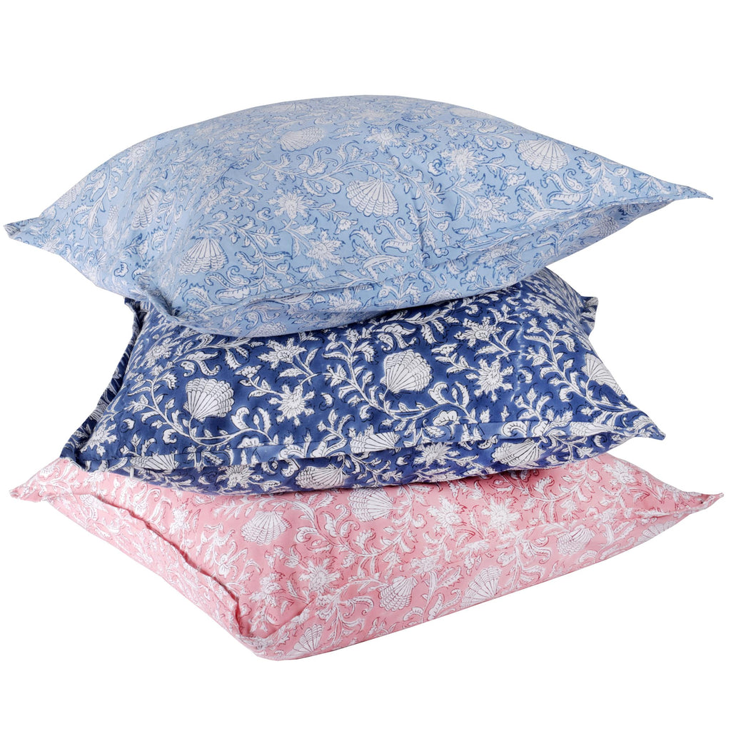 A stack of three block-printed cushions in pastel shades, featuring intricate floral and shell patterns. The top cushion is light blue, the middle one is navy blue, and the bottom one is soft pink, showcasing a harmonious blend of colors and detailed designs
