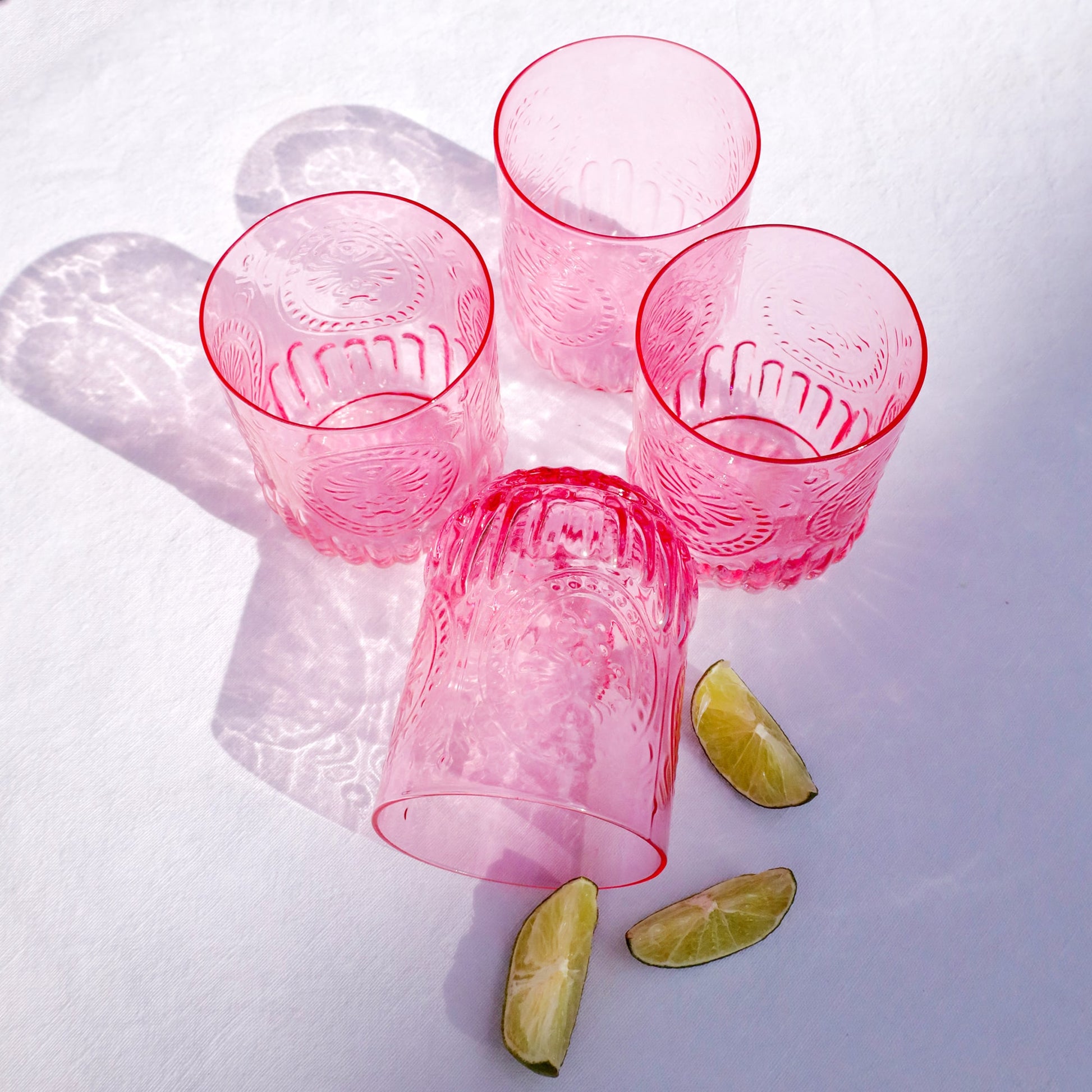 Pink glass tumblers with embossed designs on a white background with lime wedges.