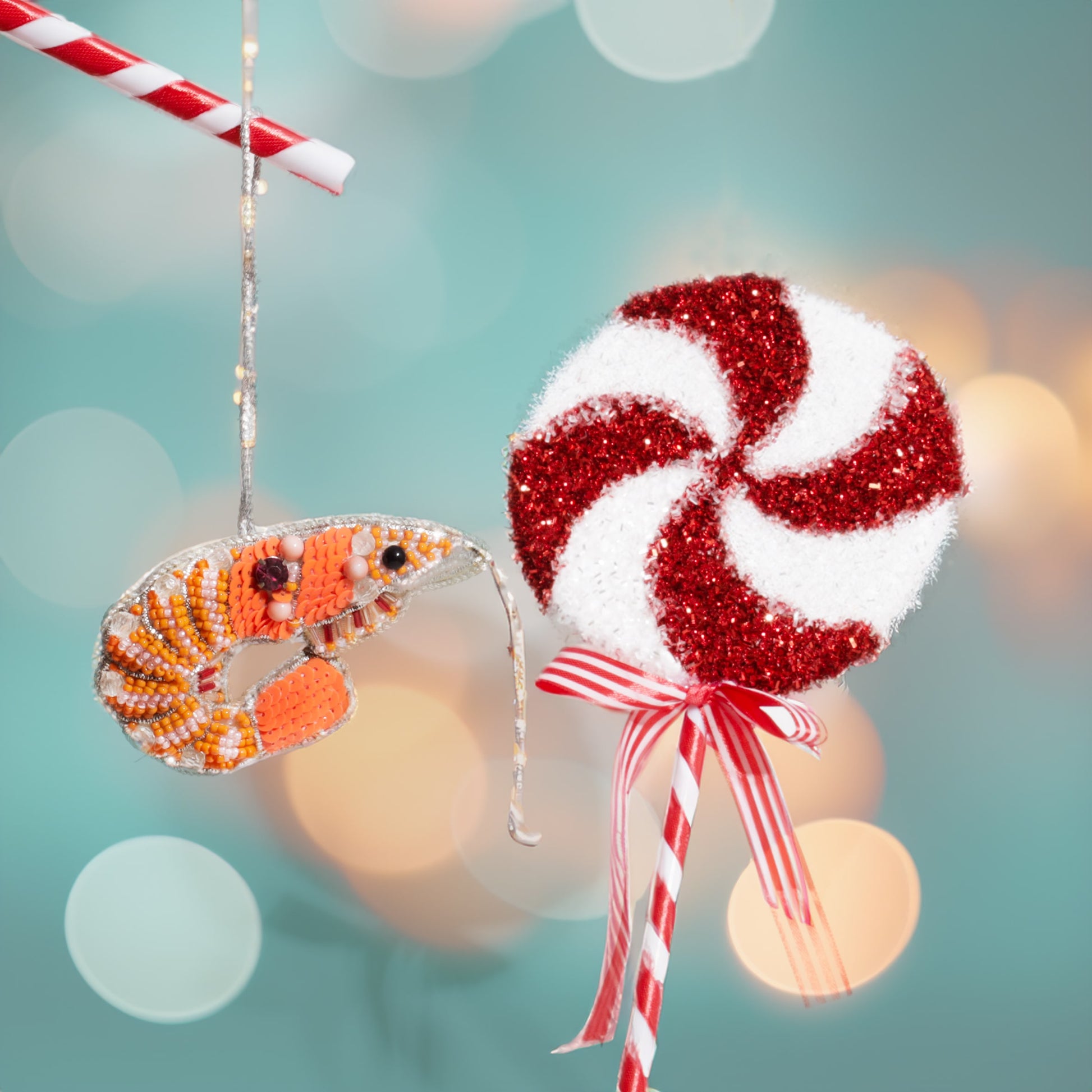 Decorative Christmas ornaments including a red and white striped candy cane and an orange and black lobster on a blurred festive background.