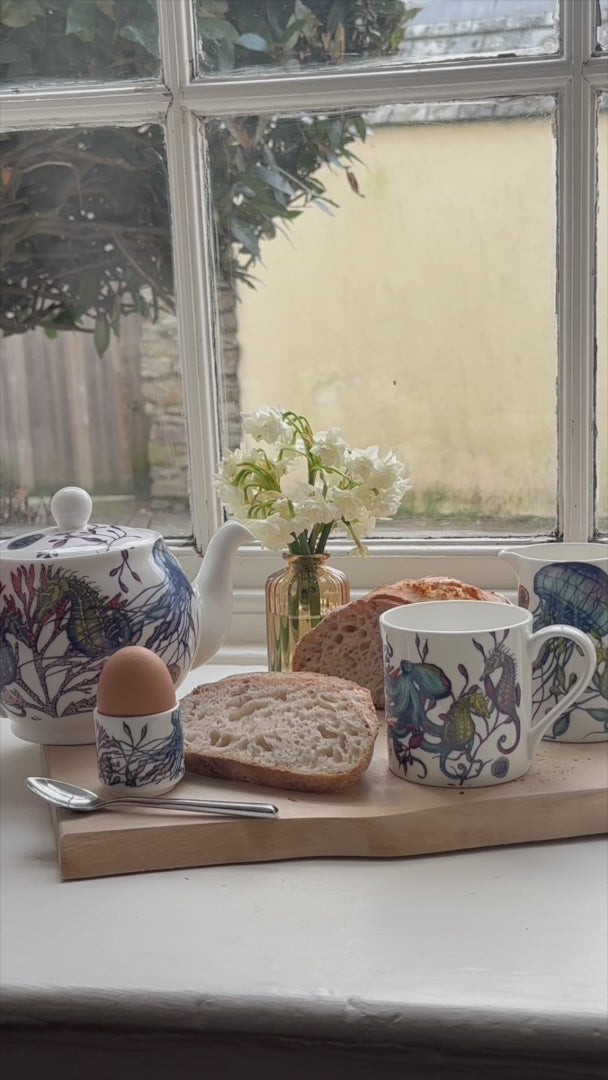 reef teapot, mug & jug on windowsill pouring and making a cup of tea for breakfast with a boiled egg and crusty bread.