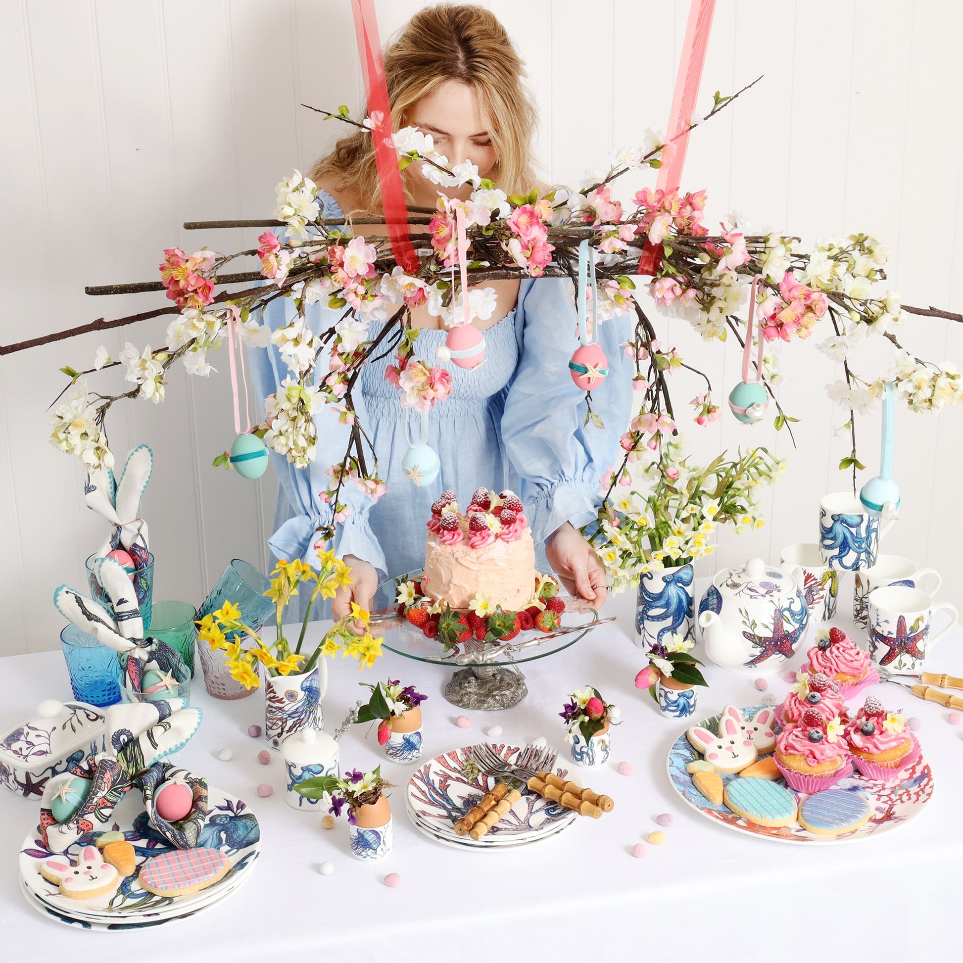 Easter table setting of the Reef tableware, and pewter octopus cake stand at the centre with frosted cake and raspberries and strawberries. Also on the table is a reef jug and a decorative spring blossom bower and decorated eggs.
