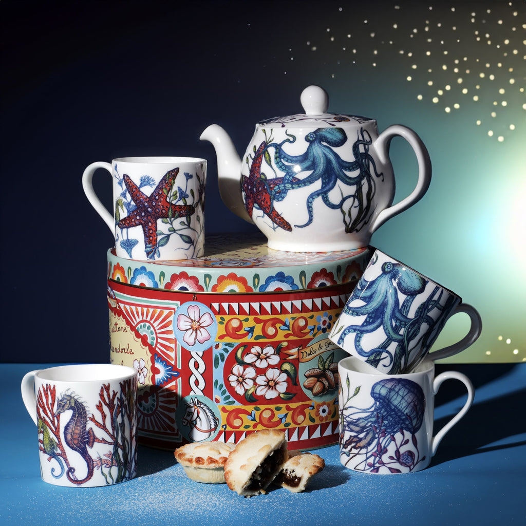 Reef collection teapot and mugs featuring sea creatures like octopus, seahorse, jellyfish, and starfish, styled with a decorative tin and mince pies on a blue background.