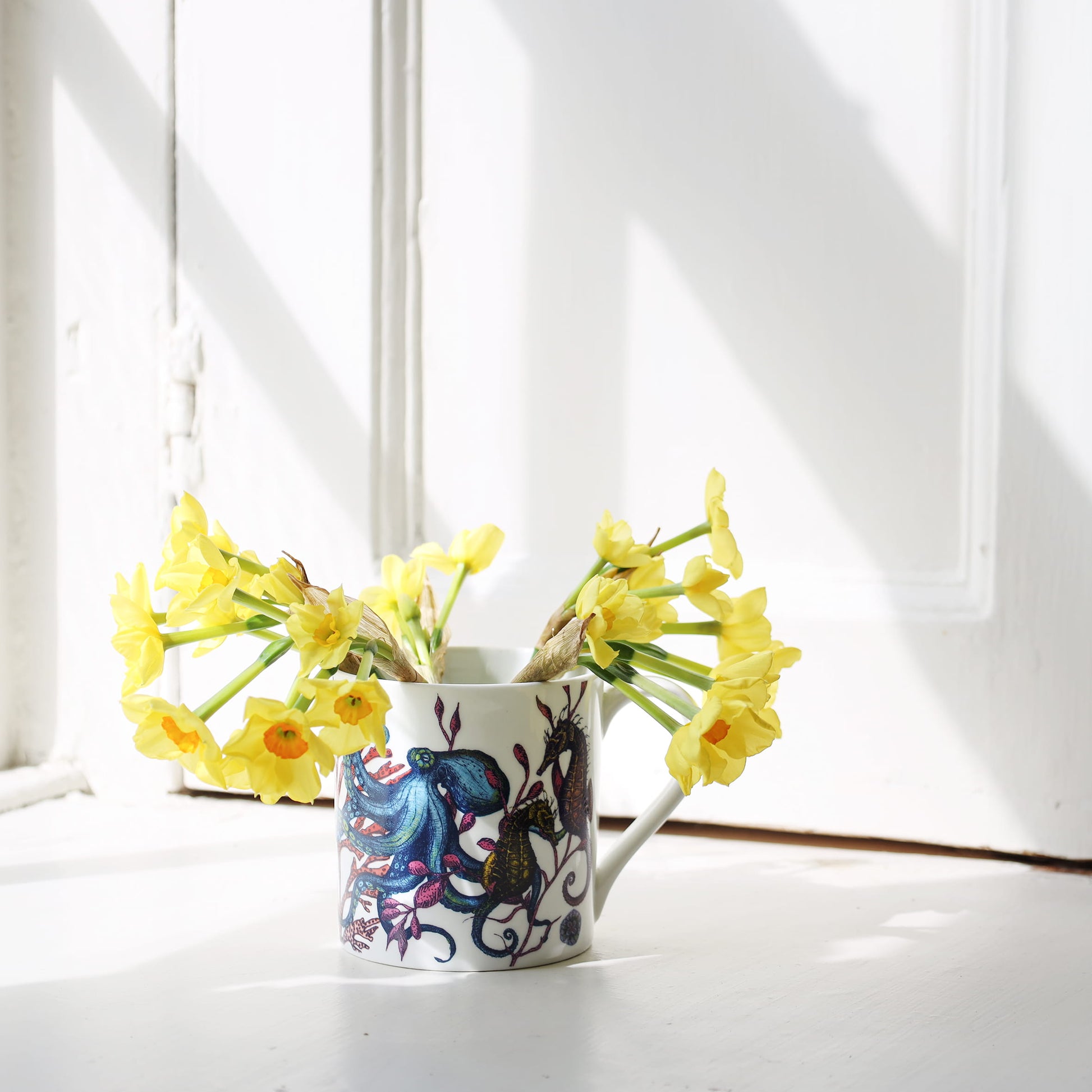 Decorative mug with reef design filled with yellow flowers on a white surface.
