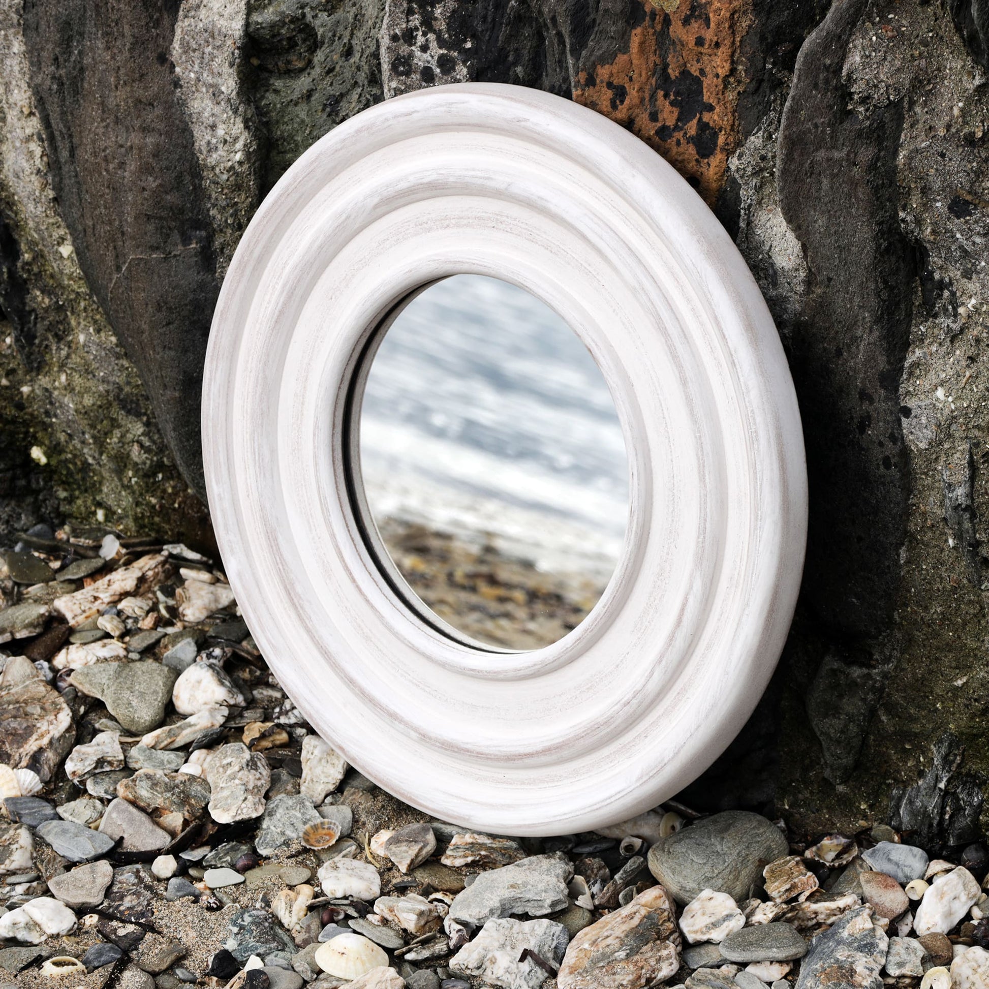 Whitewashed wooden mirror propped up against the harbour wall on the beach with the shoreline reflected in it.