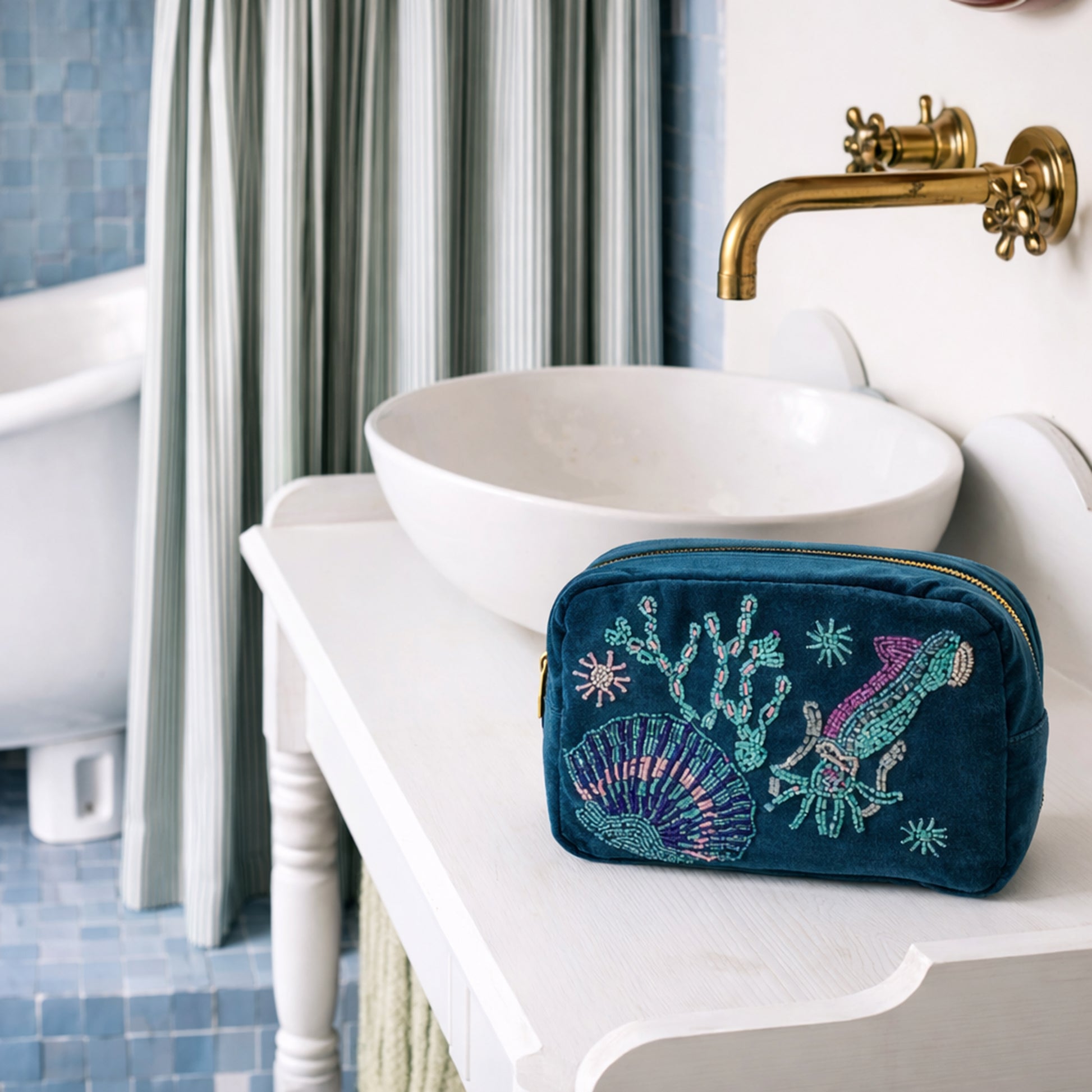 Teal  embroidered pouch on a bathroom counter with sink and bathtub in the background