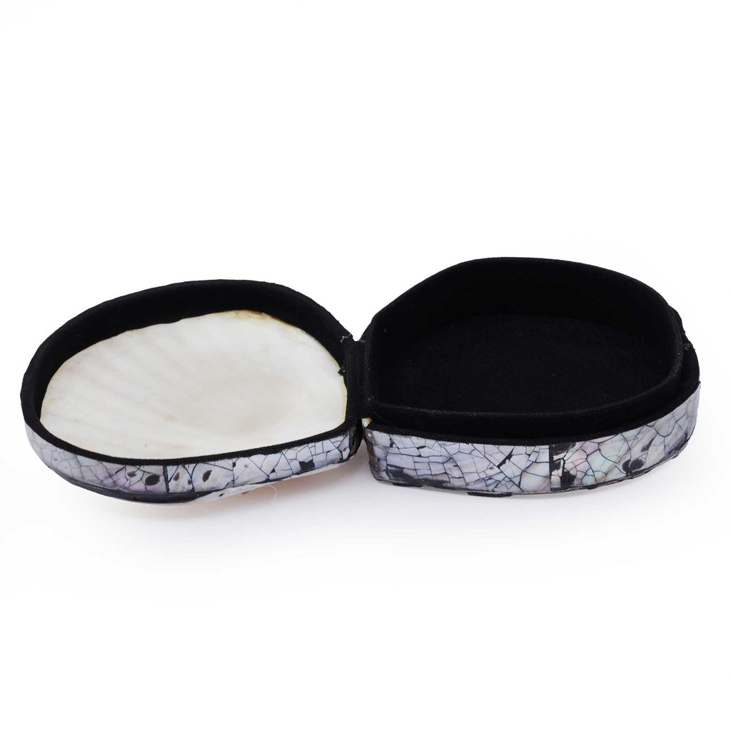 An open round jewelry box with a black velvet interior and a shell-patterned exterior featuring a white mother-of-pearl scallop shell on one side and a black-and-white crackled pattern on the other.