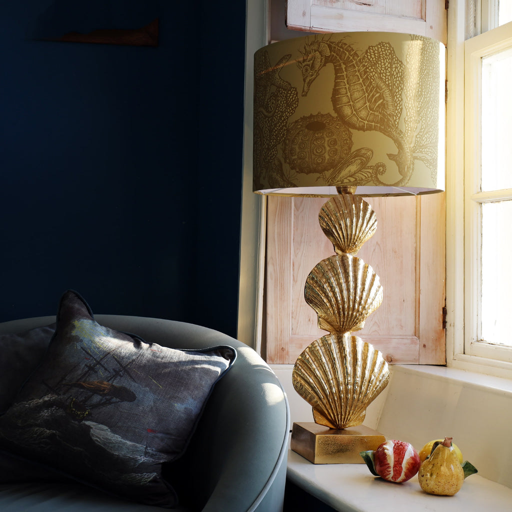 Decorative lamp with shell design on a windowsill next to a sofa with a cushion.