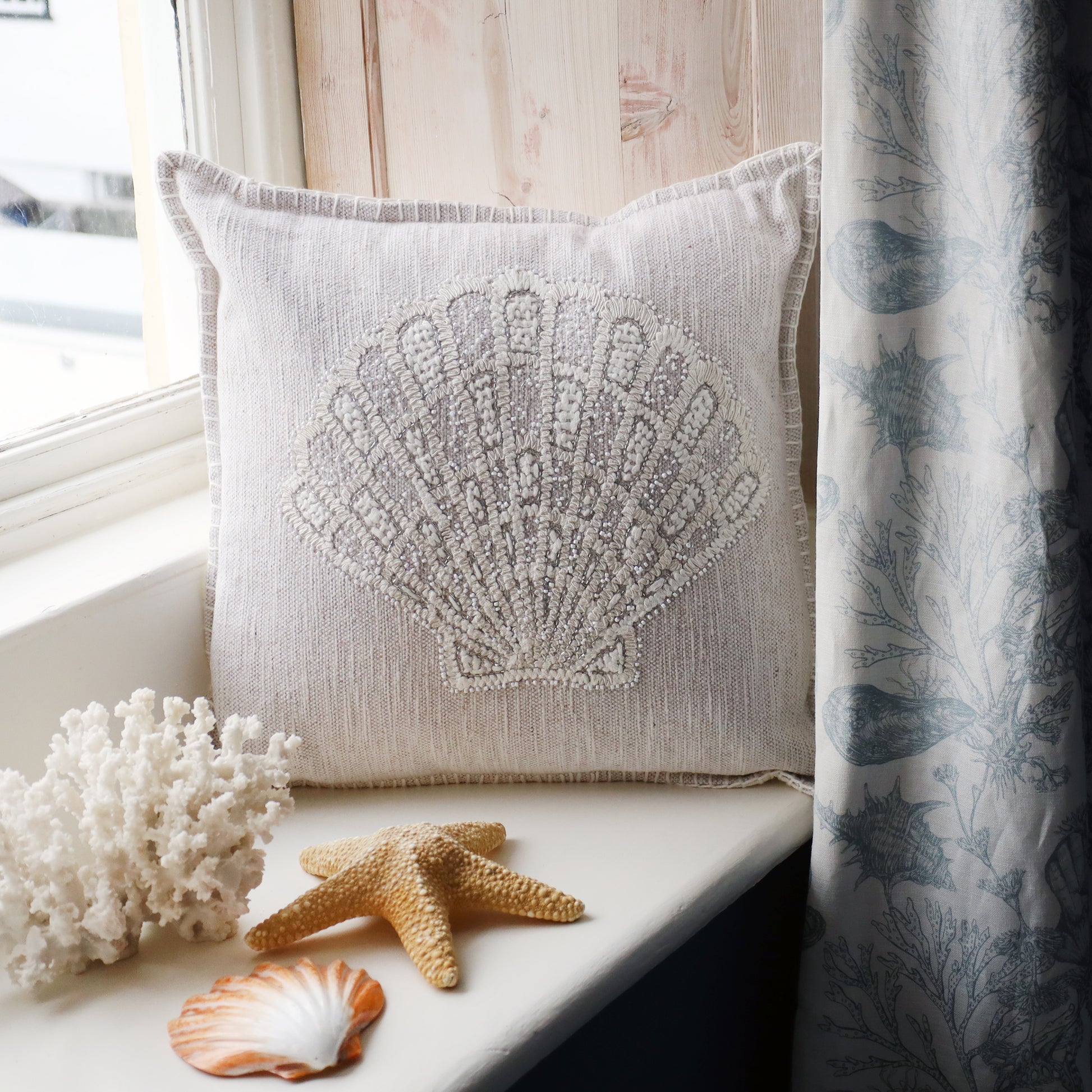 Decorative pillow with shell design on a windowsill with starfish and coral