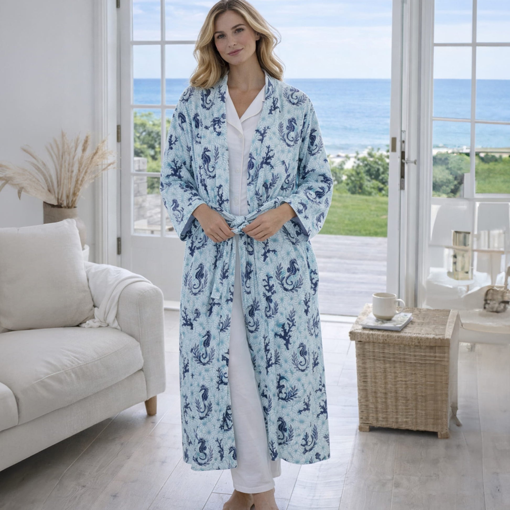 Woman wearing a blue patterned seahorse & coral robe in a bright room with large windows.
