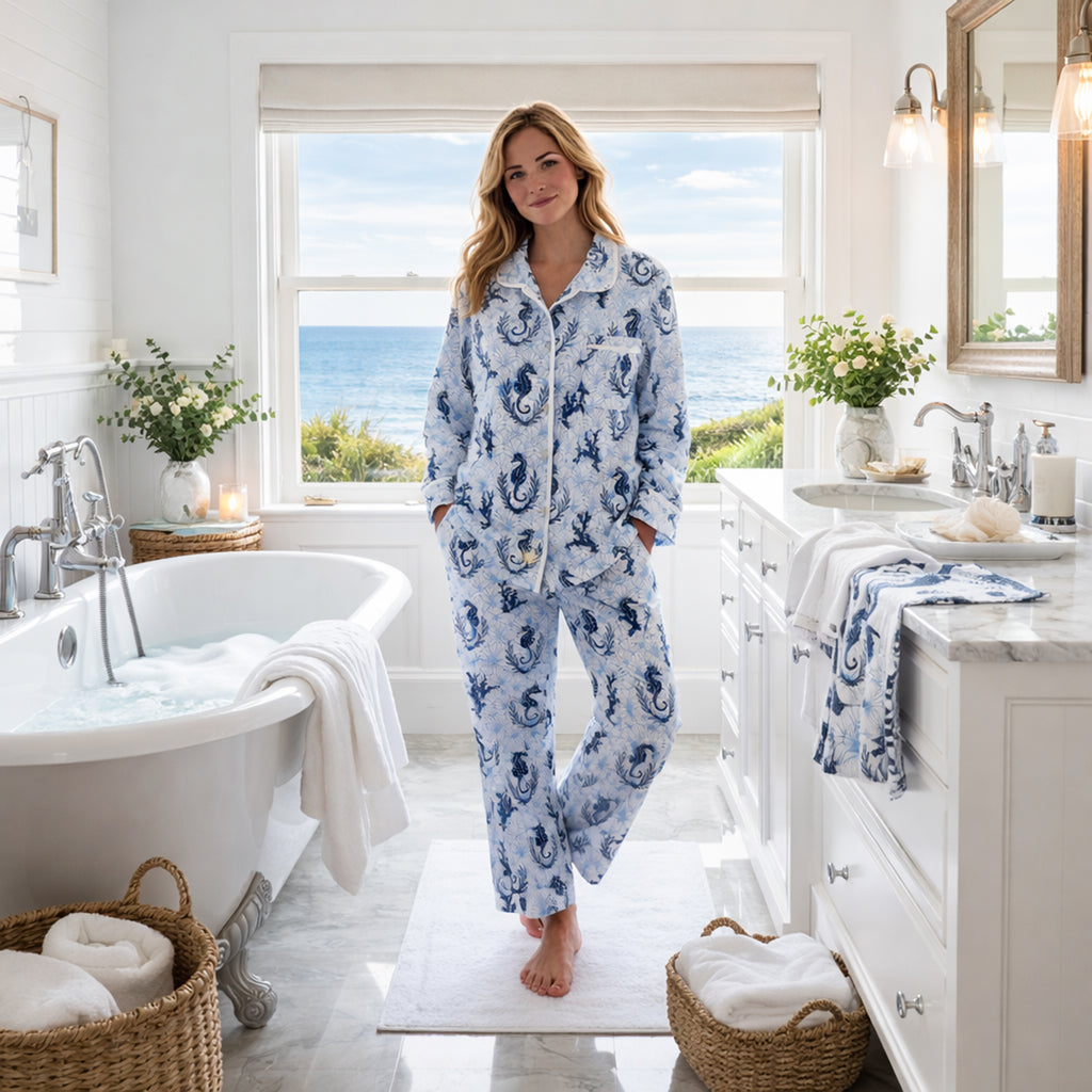 Woman in blue floral pajamas standing in a bright bathroom with ocean view