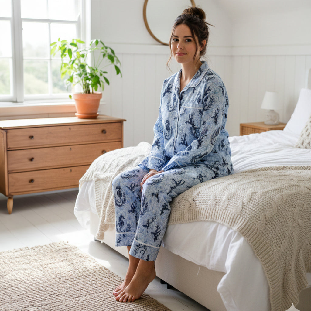 Woman in blue pajamas sitting on a bed in a bright bedroom.