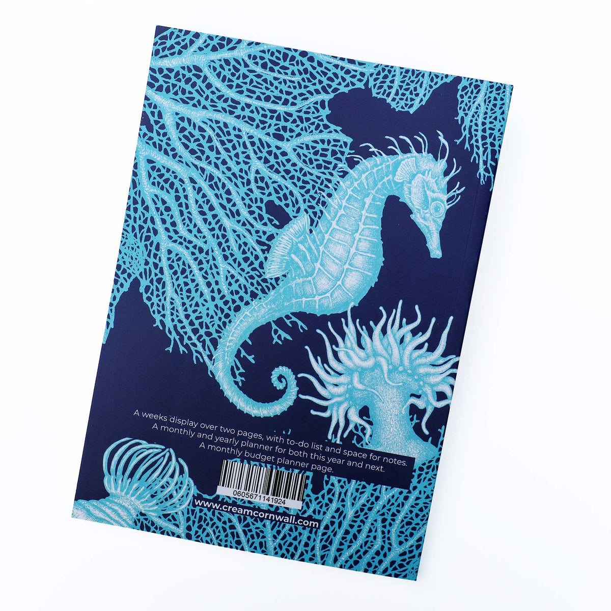 A notebook or planner shown at an angle on a white background, featuring a dark navy blue cover decorated with light blue seahorse and coral illustrations. The back cover includes descriptive text and a barcode.