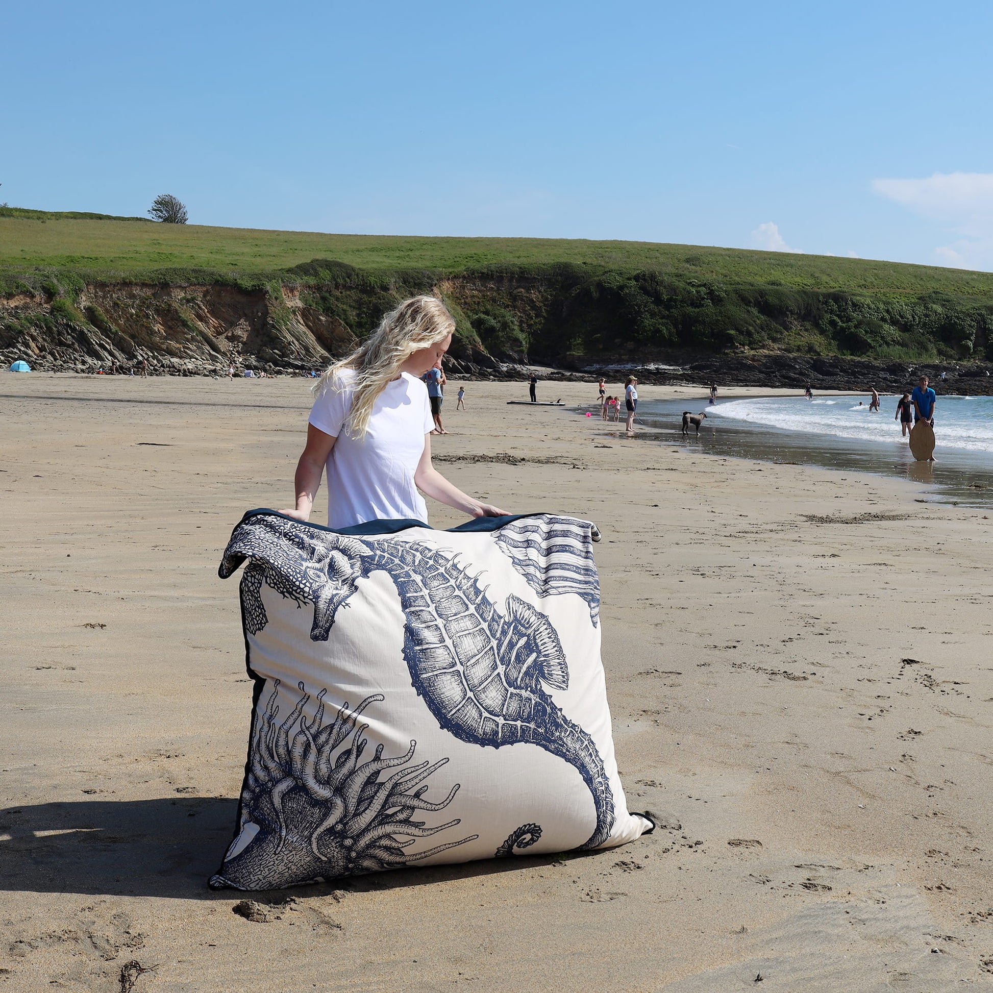 Person on a beach with a large decorative pillow featuring marine life patterns.