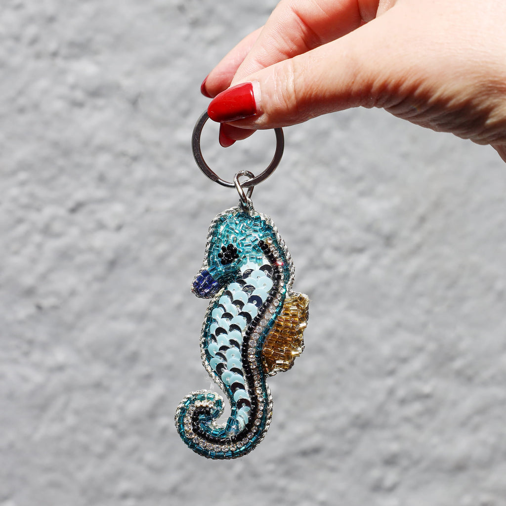 Hand holding a seahorse-shaped keychain against a gray background