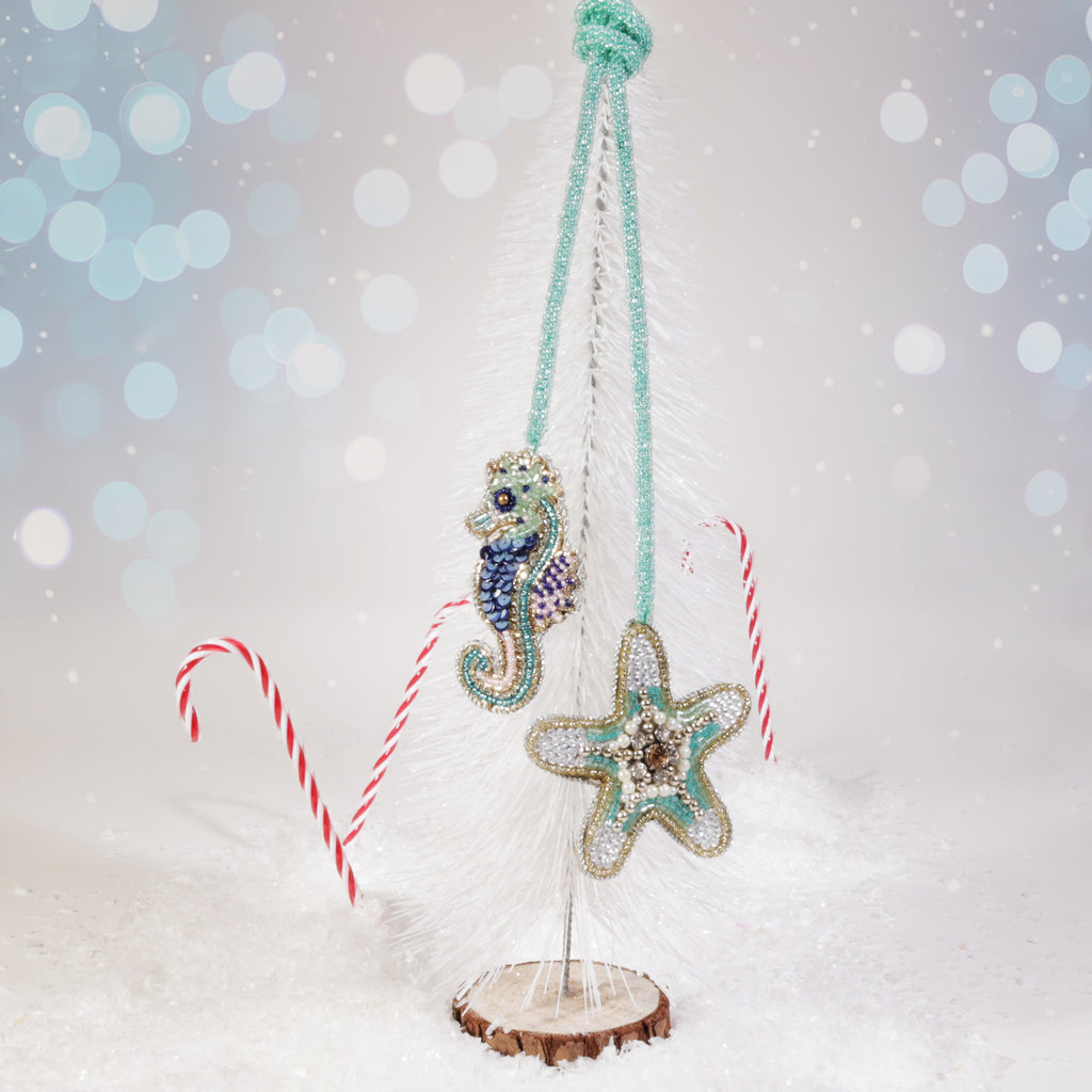 Beaded seahorse and starfish bag charms in turquoise, blue, and gold hanging from a white miniature Christmas tree, surrounded by snow and candy canes on a festive background.