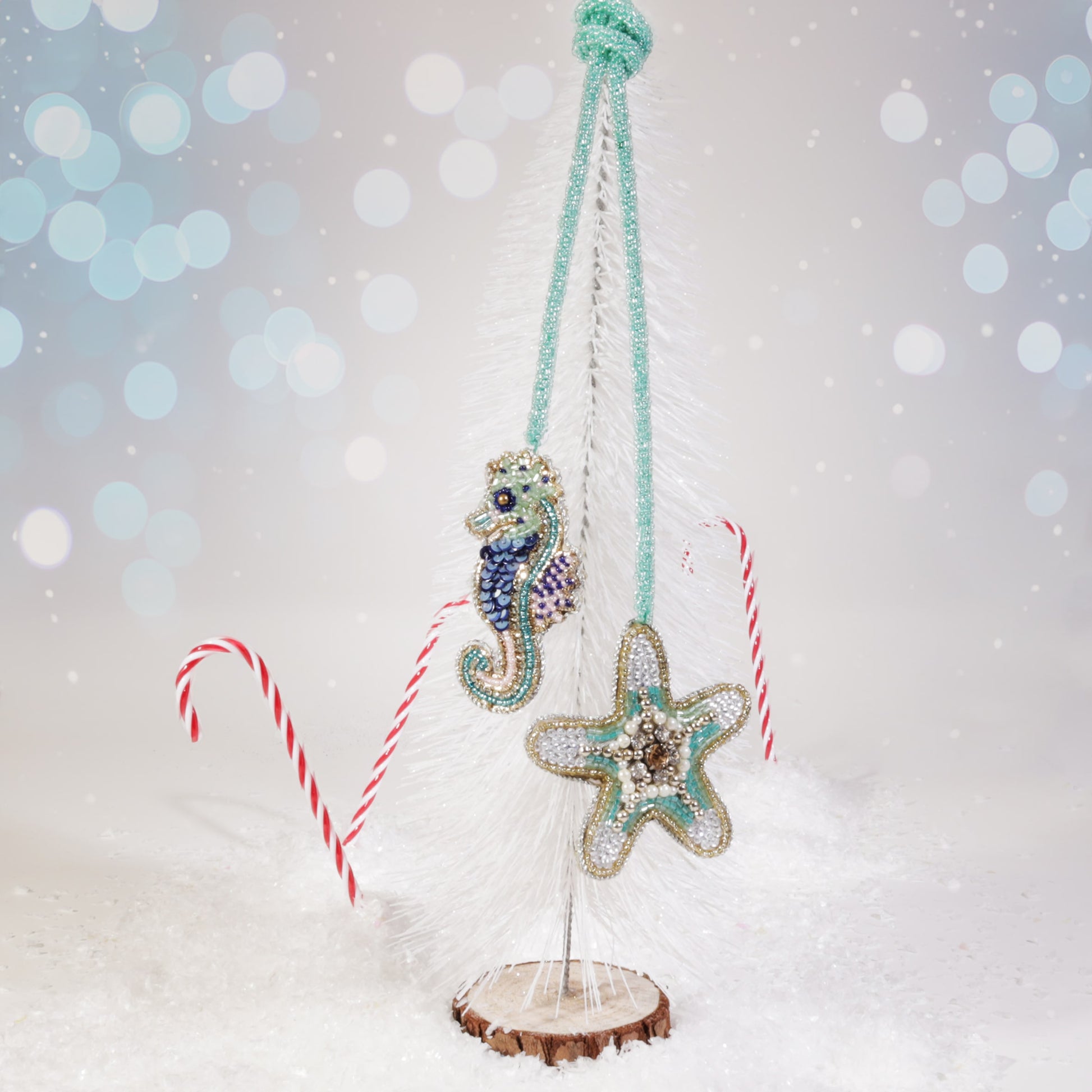 Beaded seahorse and starfish bag charms in turquoise, blue, and gold hanging from a white miniature Christmas tree, surrounded by snow and candy canes on a festive background.