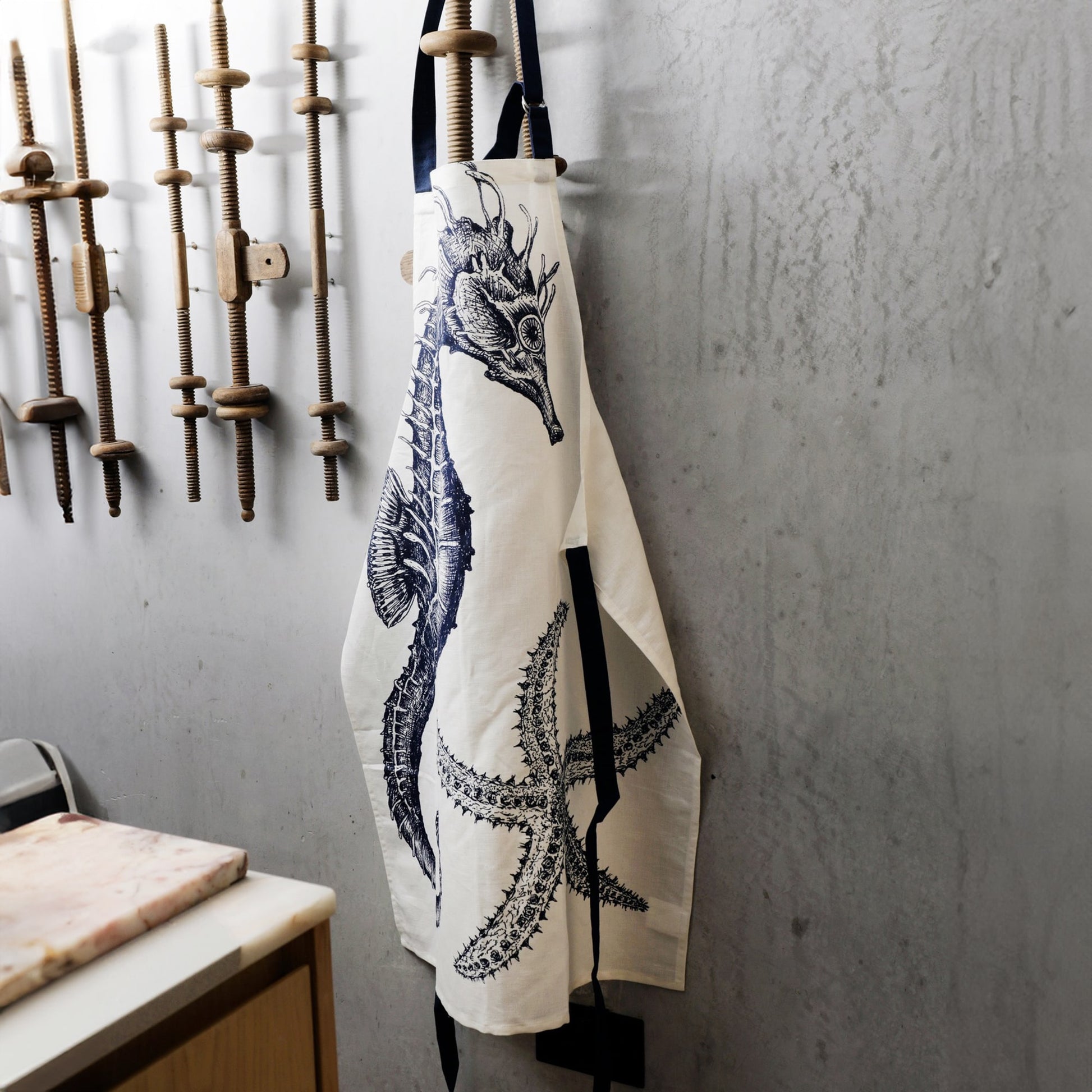 Apron with a seahorse & starfish design hanging on a wall with tools.