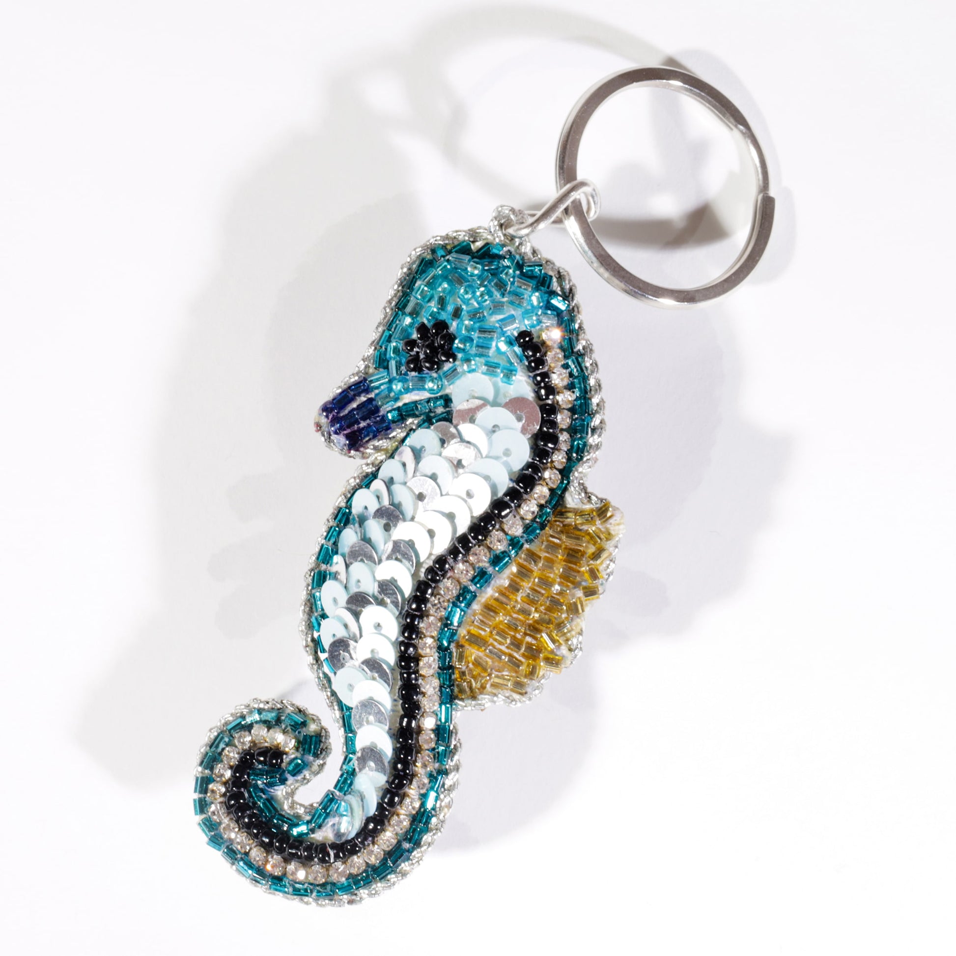A beaded seahorse keyring featuring turquoise, silver, gold, and black sequins with a metallic keyring attachment, photographed on a white background.