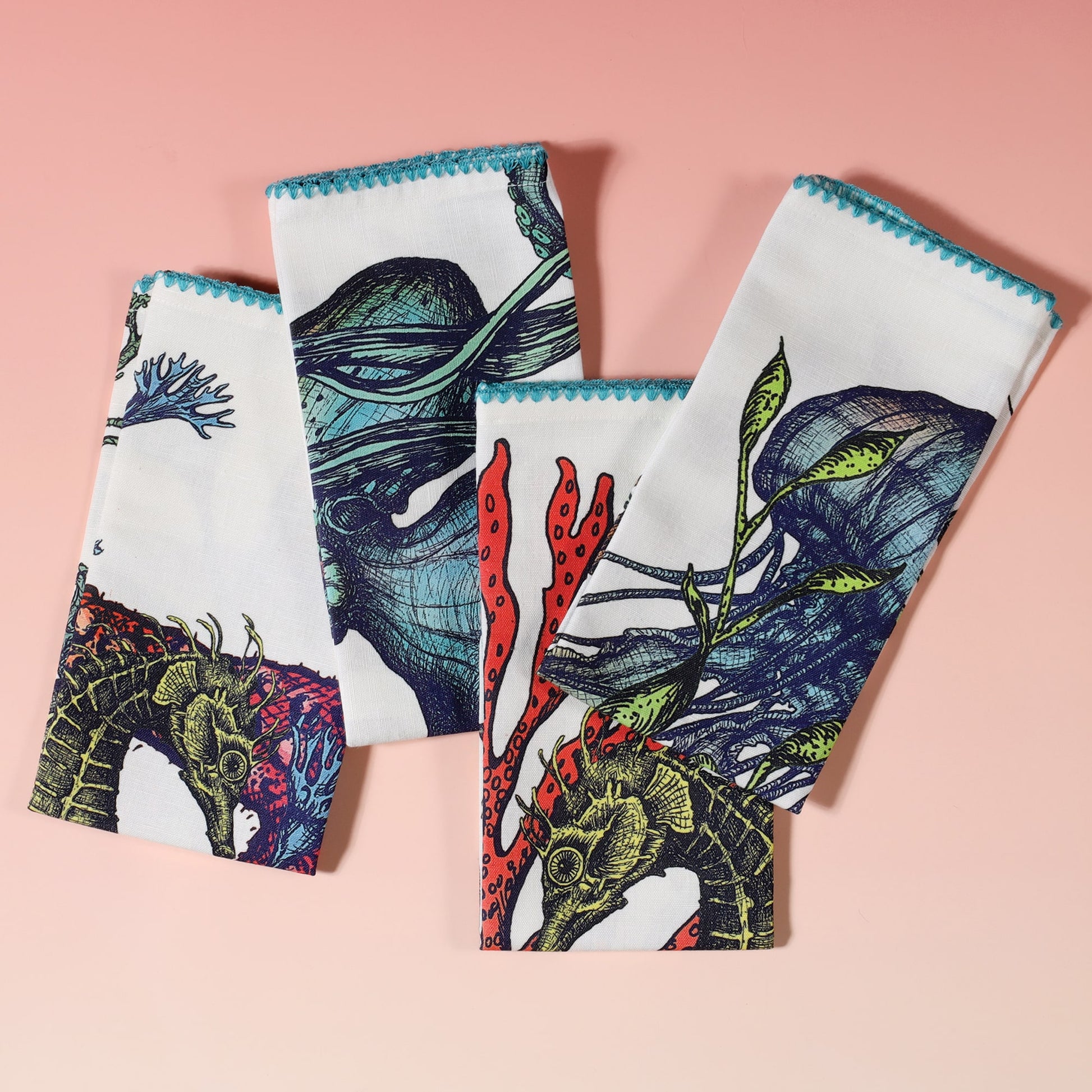 set of 4 brightly coloured off white linen napkins with hand drawn seahorse, starfish, octopus and jellyfish illustrations and turquoise scallop edged embroidery folded on top of each other