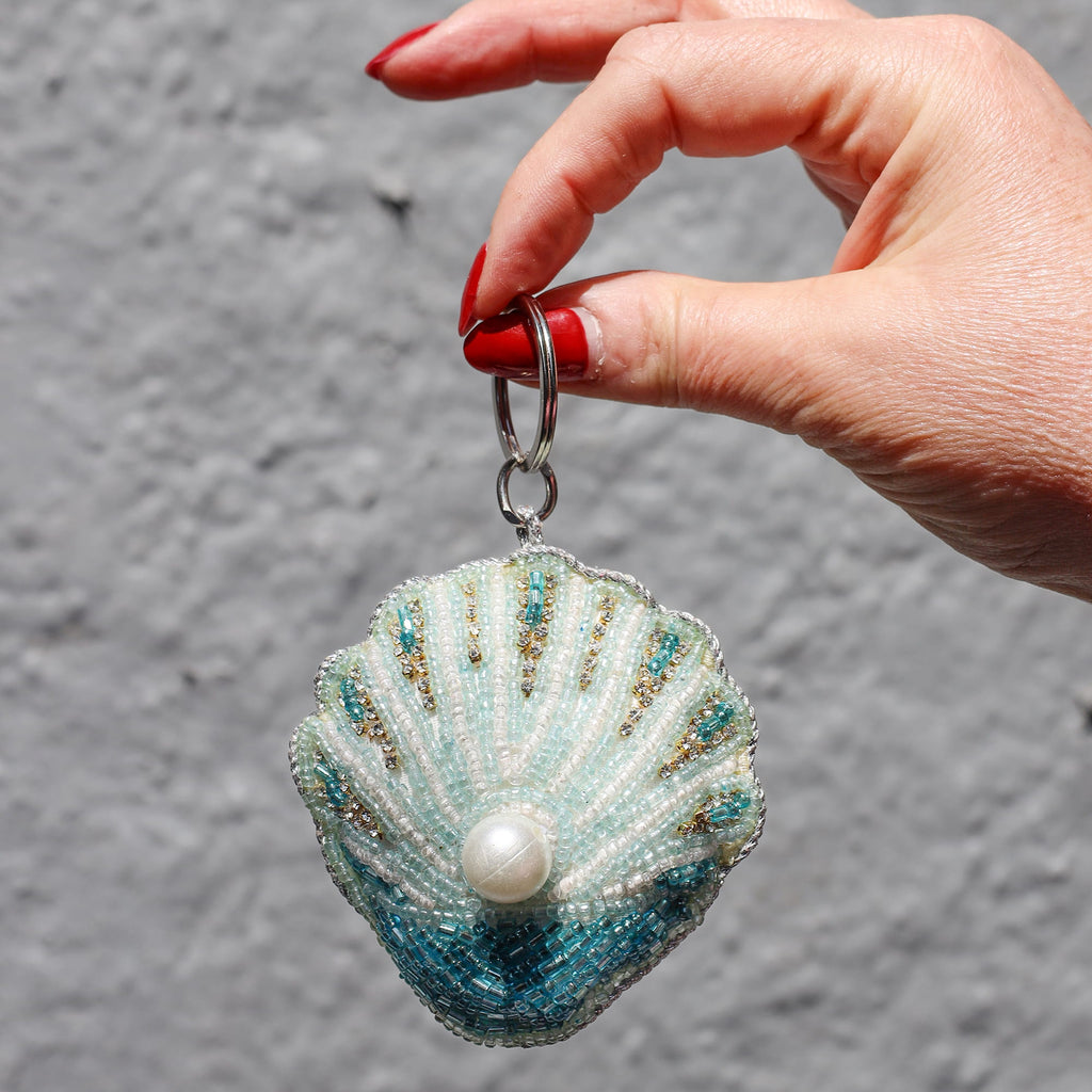 Hand holding a shell-shaped keychain with a pearl on a gray background