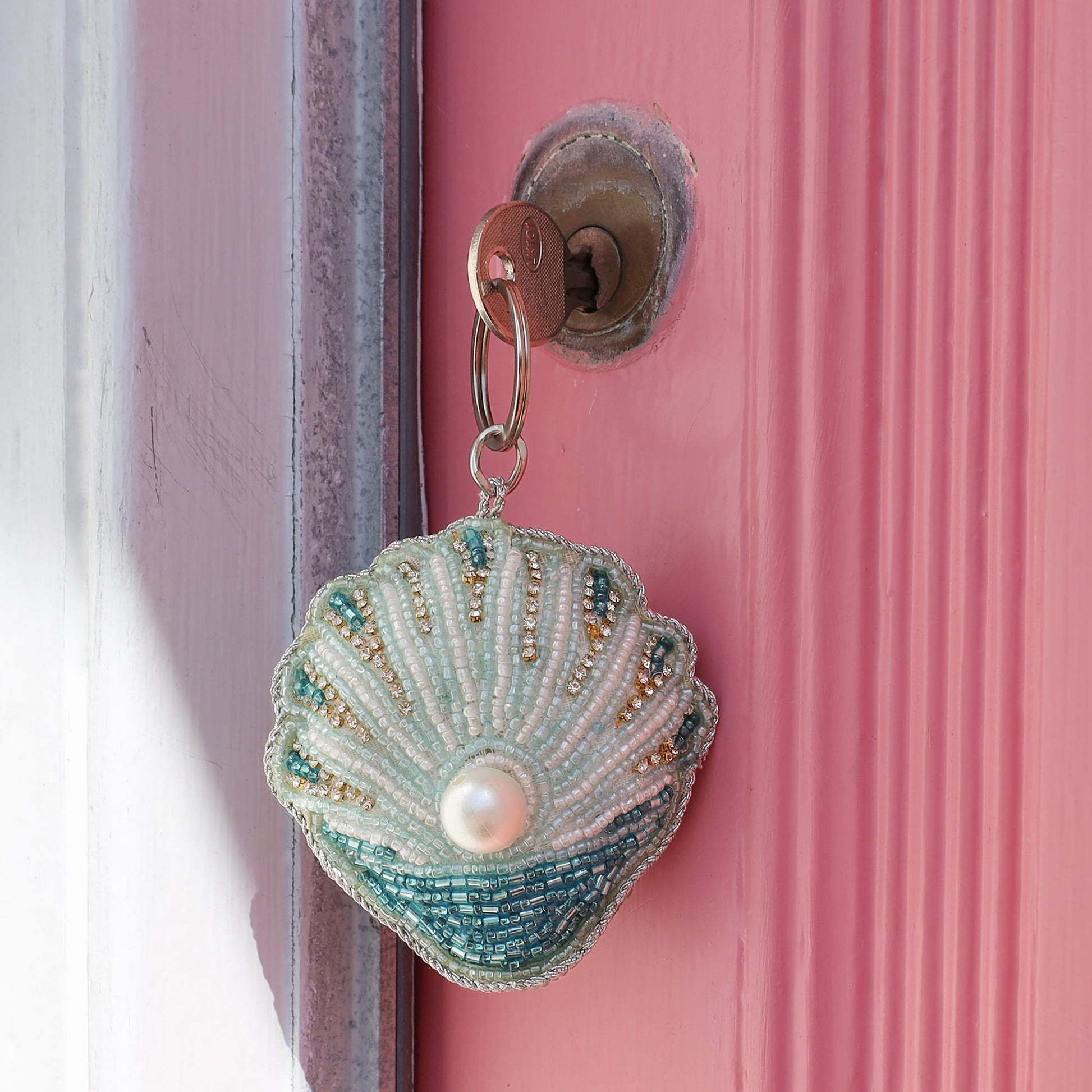 Decorative keychain shaped like a shell with beads on a pink door.
